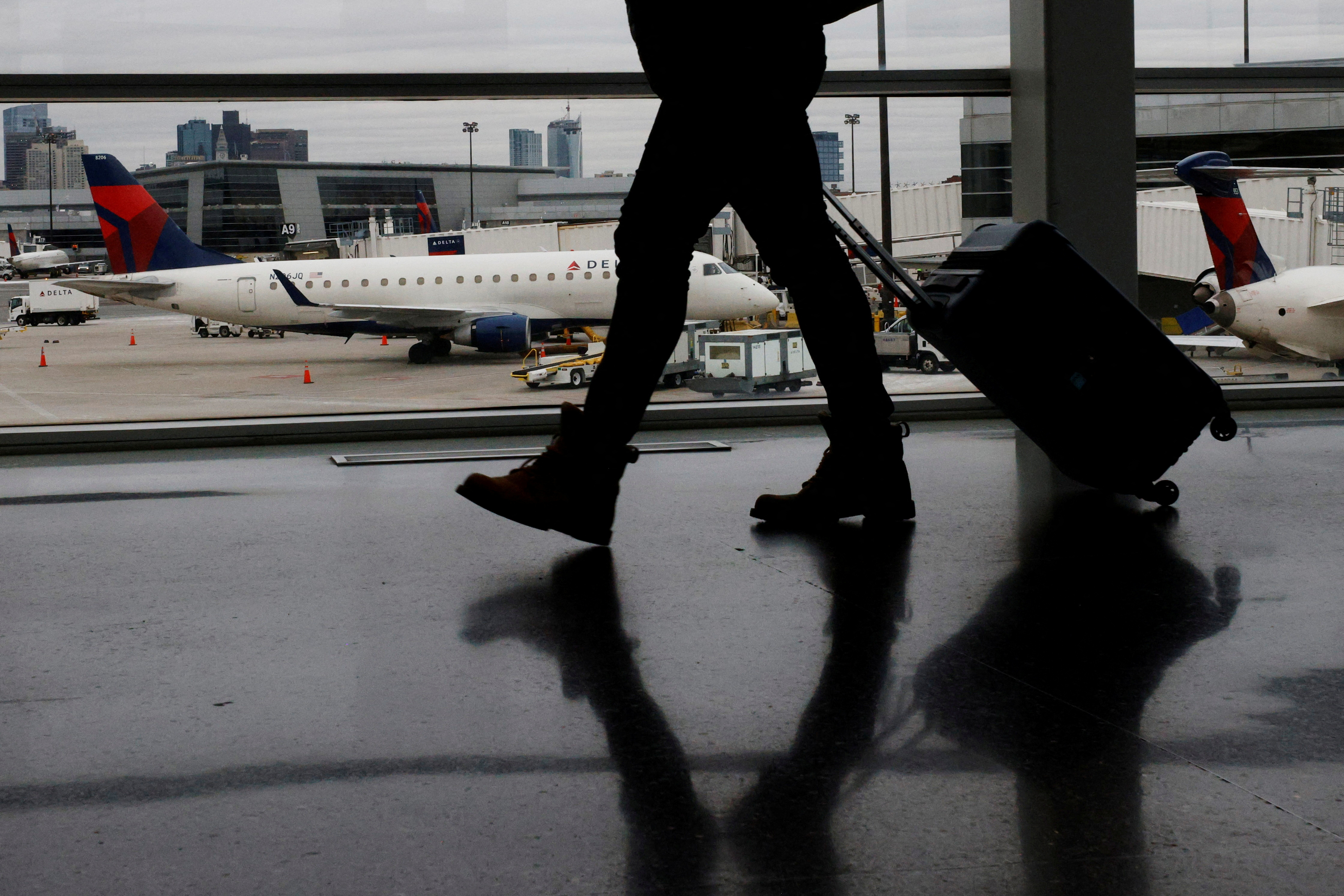 A passenger walks past a Delta Airlines plane at a gate at Logan International Airport in Boston
