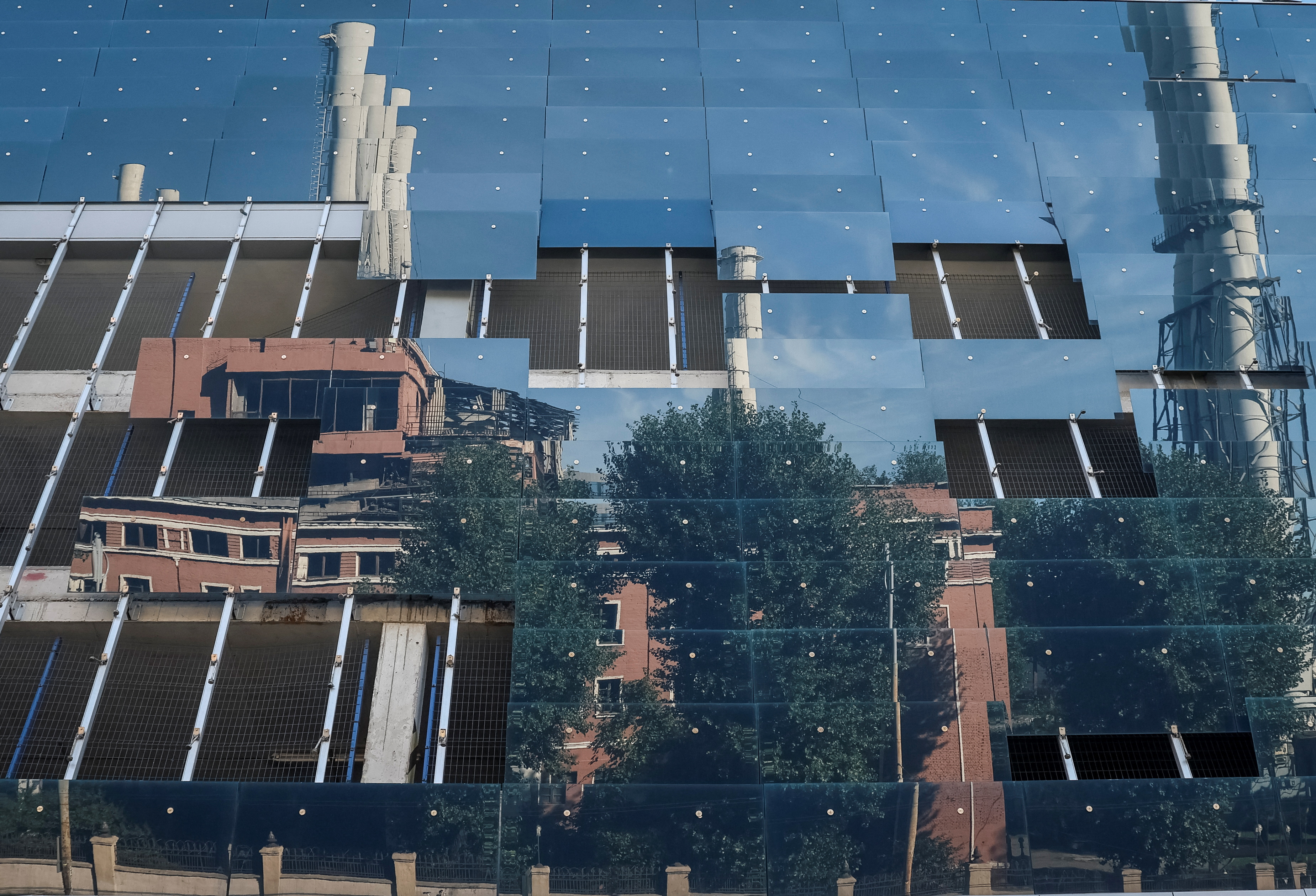 Usina térmica danificada é refletida nas janelas restantes de um centro de negócios danificado após o ataque militar russo do dia anterior, enquanto a invasão da Ucrânia pela Rússia continua, no centro de Kyiv