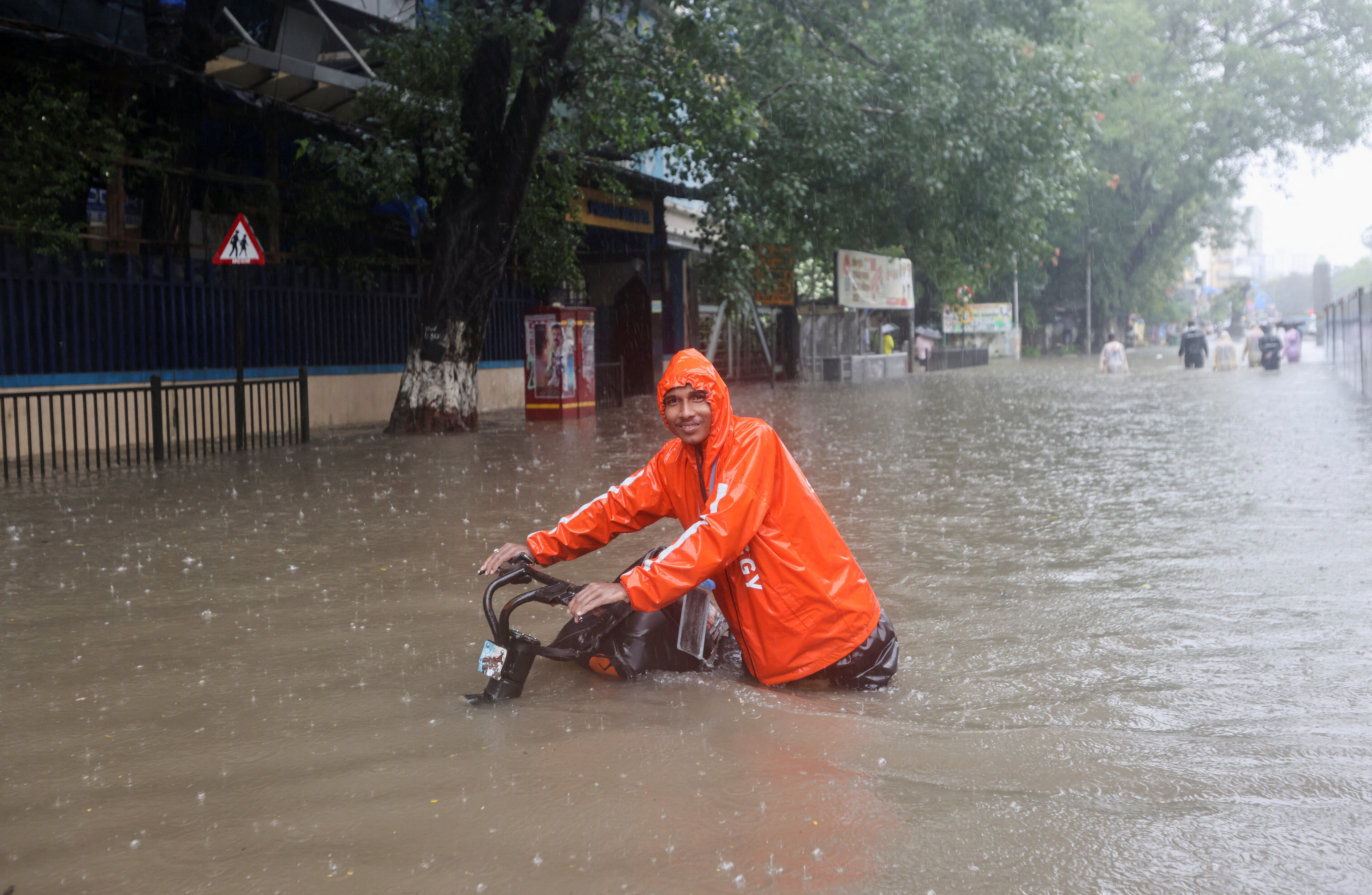 A man wades through a flooded street with his bike amidst heavy rainfall in Mumbai