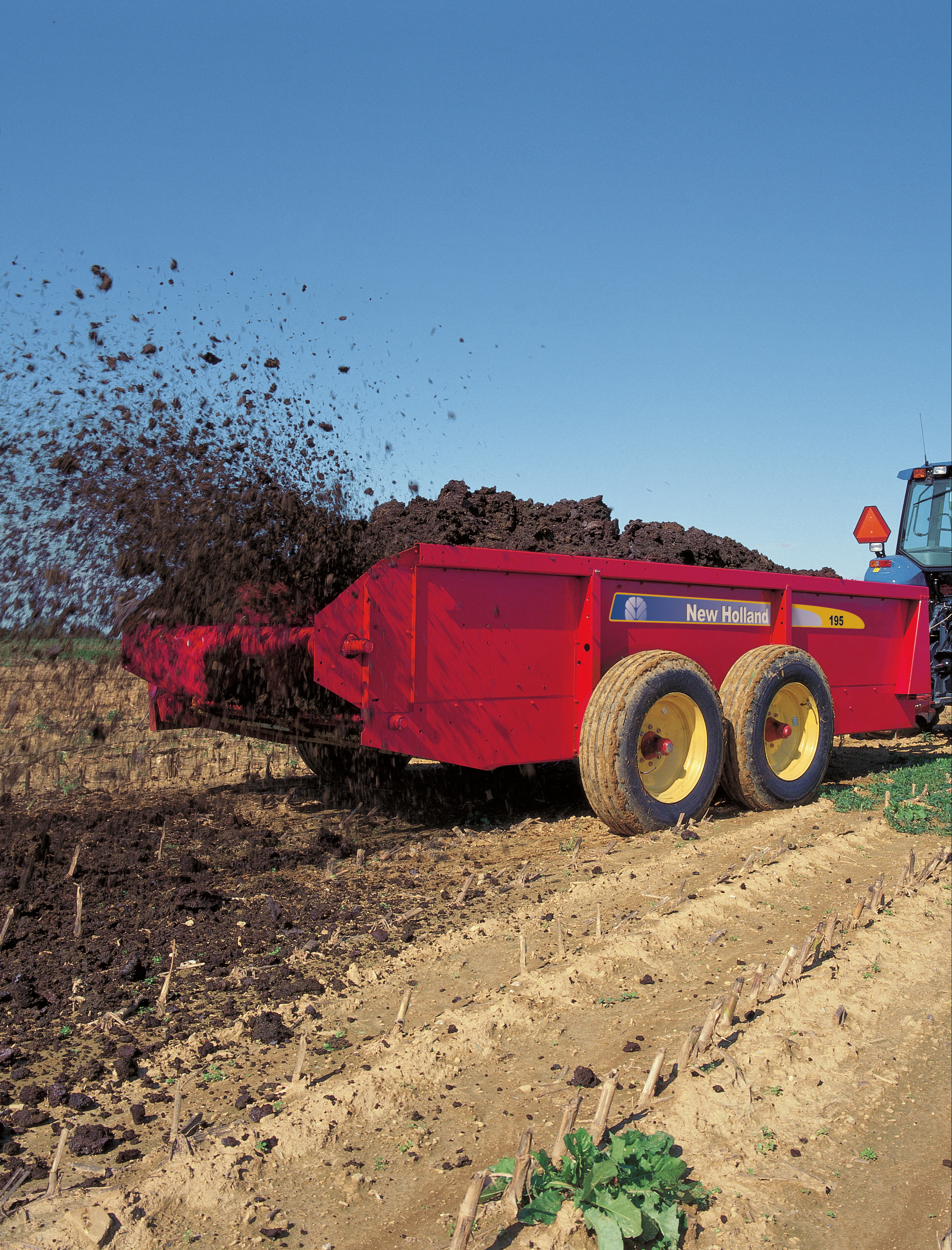 A New Holland Agriculture 100 series box spreader distributes solid manure on a farm field in Rising Sun