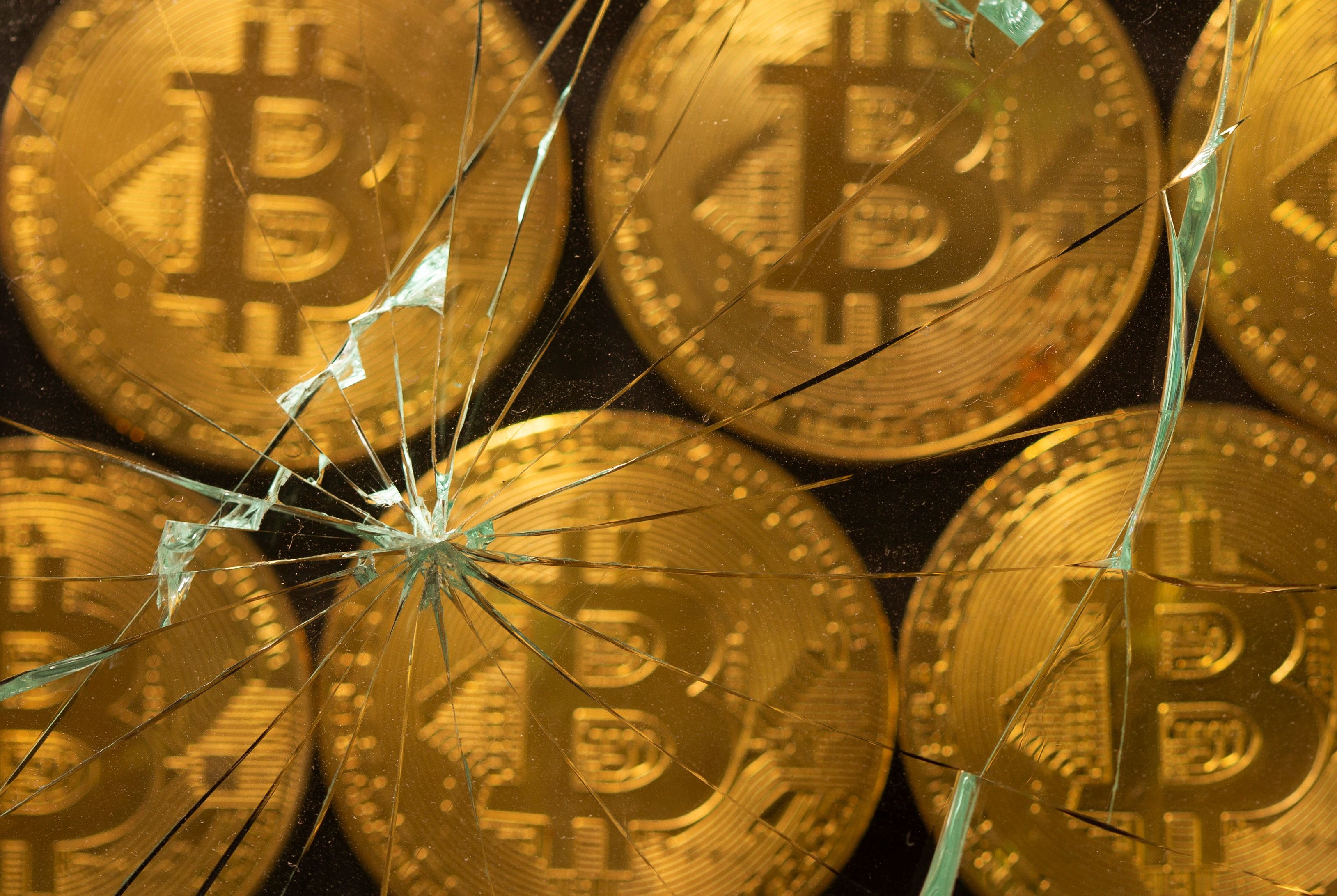 Representations of virtual currency bitcoin are seen through broken glass in this illustration taken