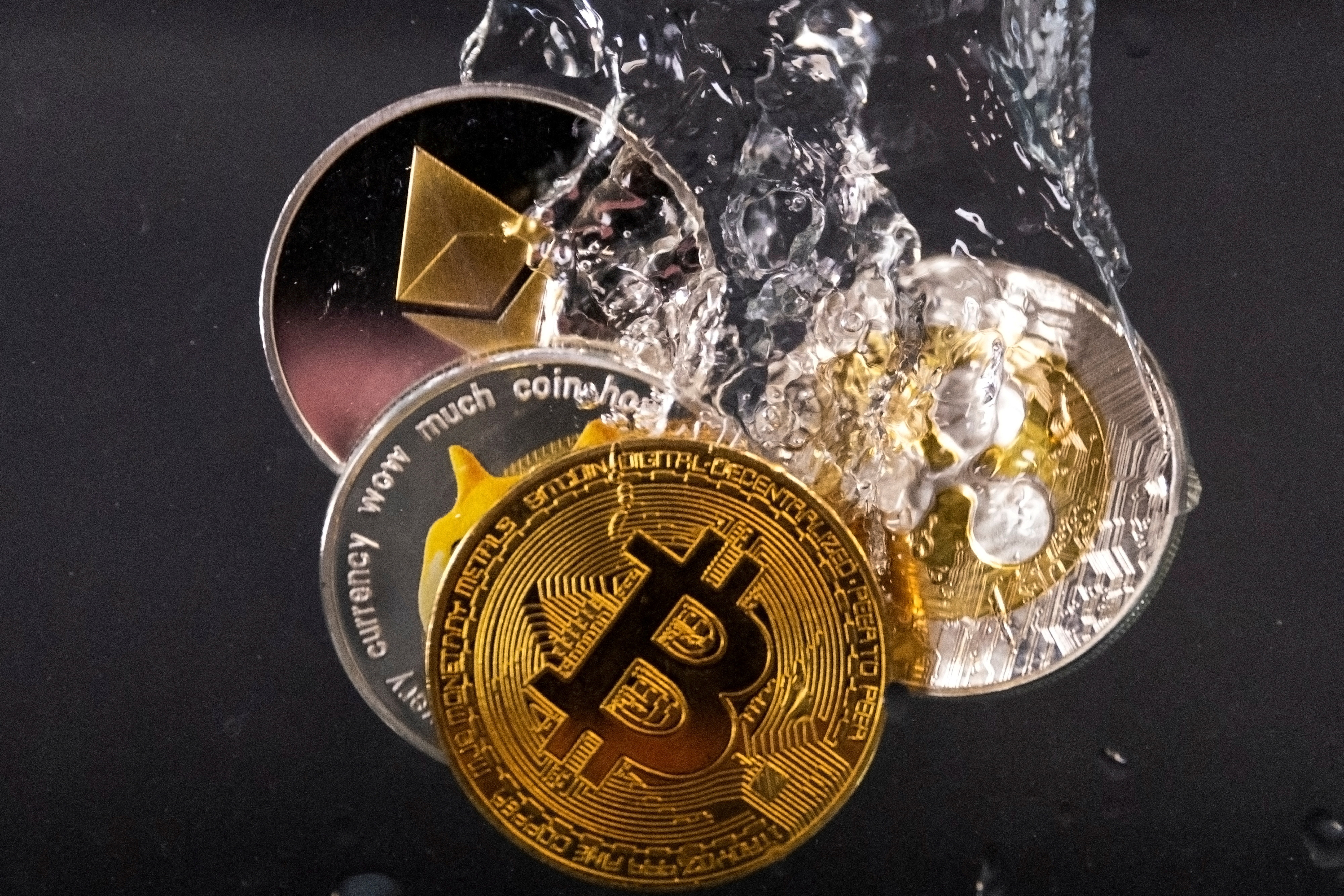 Commemorative tokens representing Bitcoin, Ethereum, Dogecoin and Ripple cryptocurrency networks are immersed in water