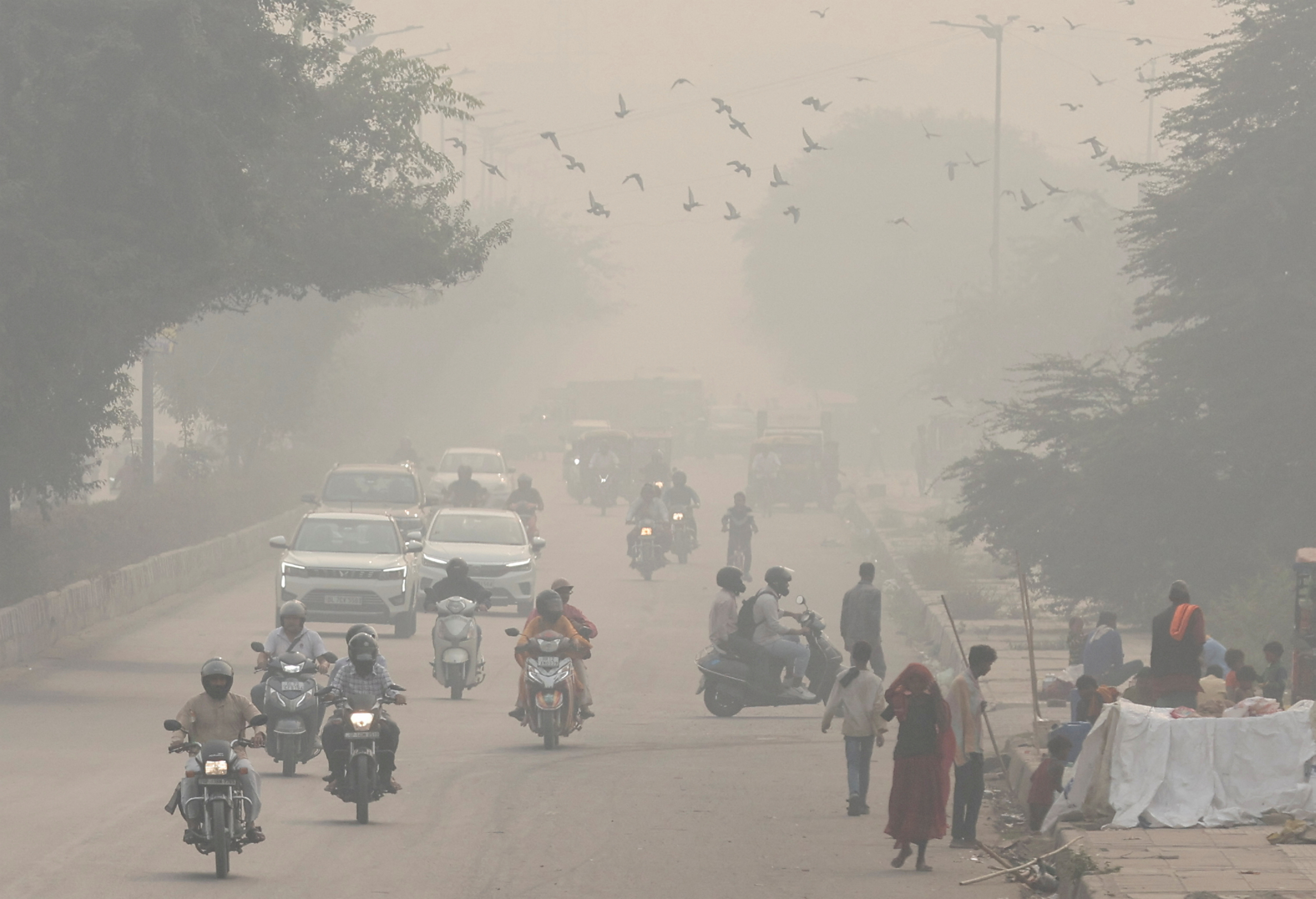 People and vehicles are seen on a road amidst the morning smog in New Delhi