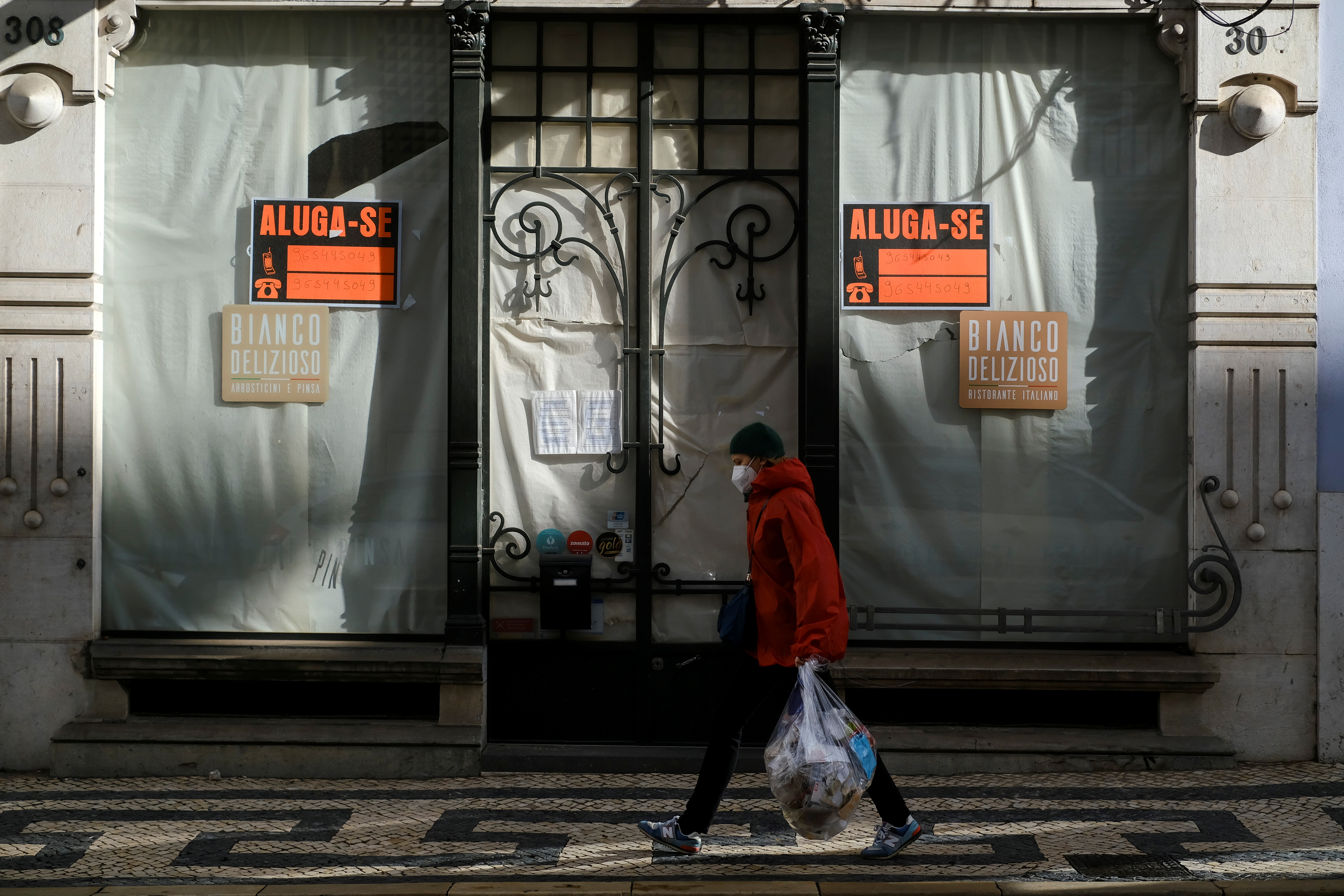 A woman wearing a protective mask due to coronavirus disease (COVID-19) pandemic walks past a closed store in central Lisbon, Portugal, November 25, 2021. REUTERS/Pedro Nunes