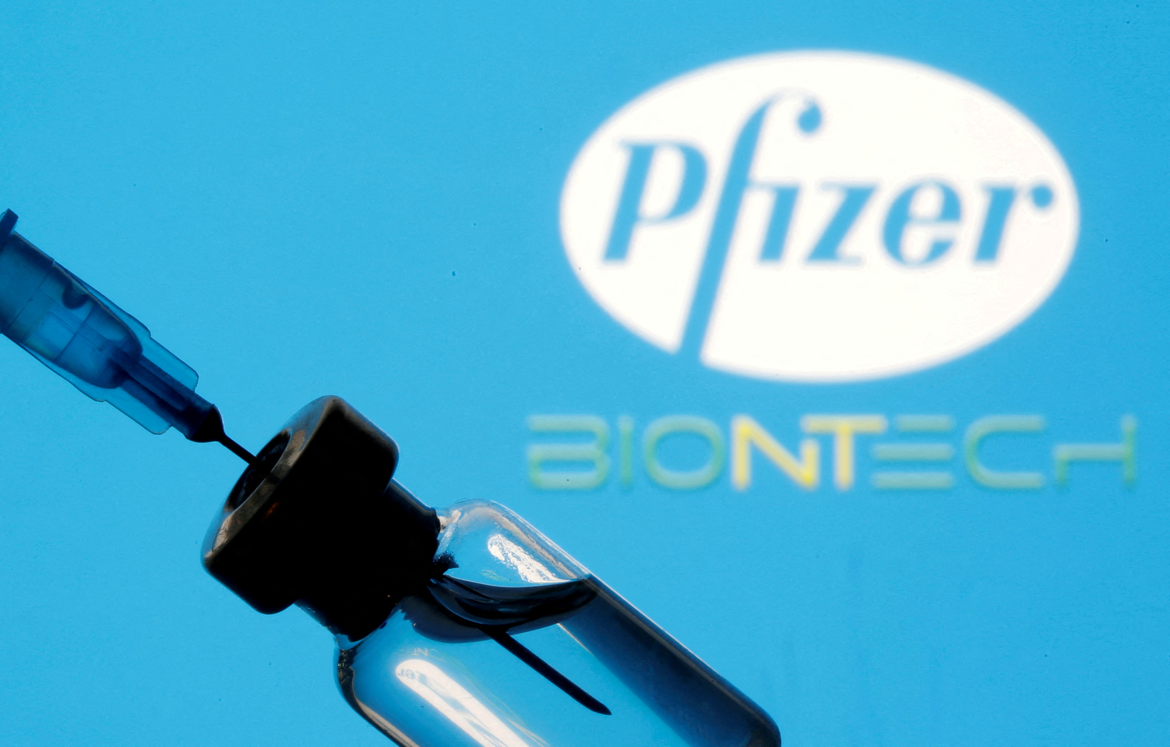 Vial and sryinge are seen in front of displayed Pfizer and Biontech logo