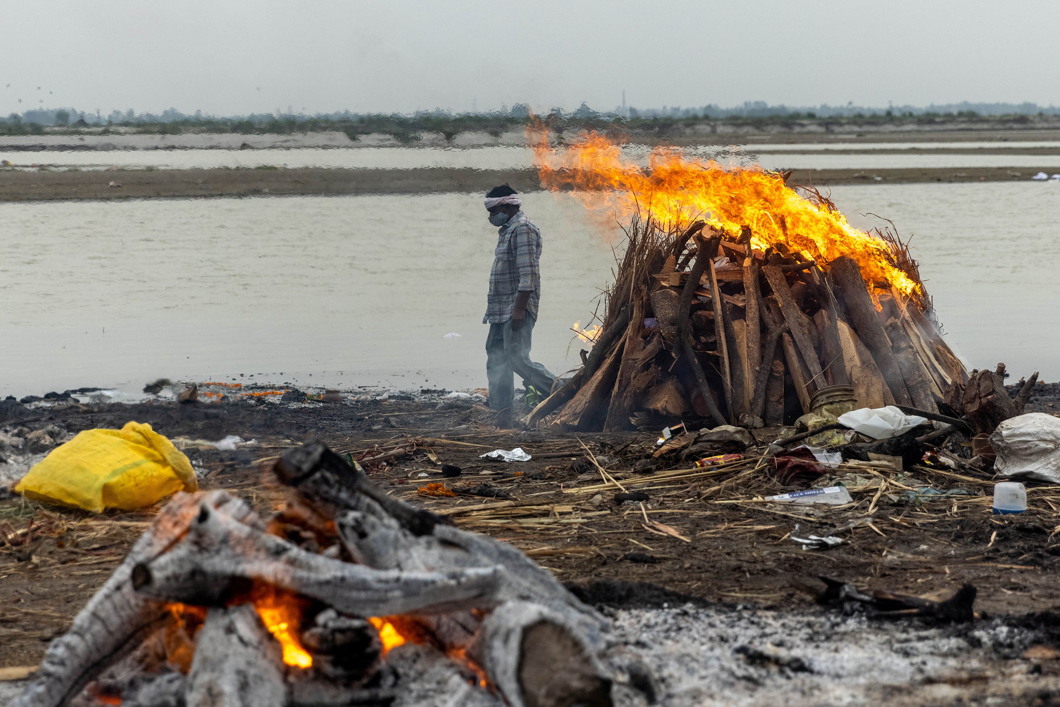 A man walks past burning pyres with people who died from the coronavirus disease (COVID-19), on the banks of the river Ganges at Garhmukteshwar in the northern state of Uttar Pradesh