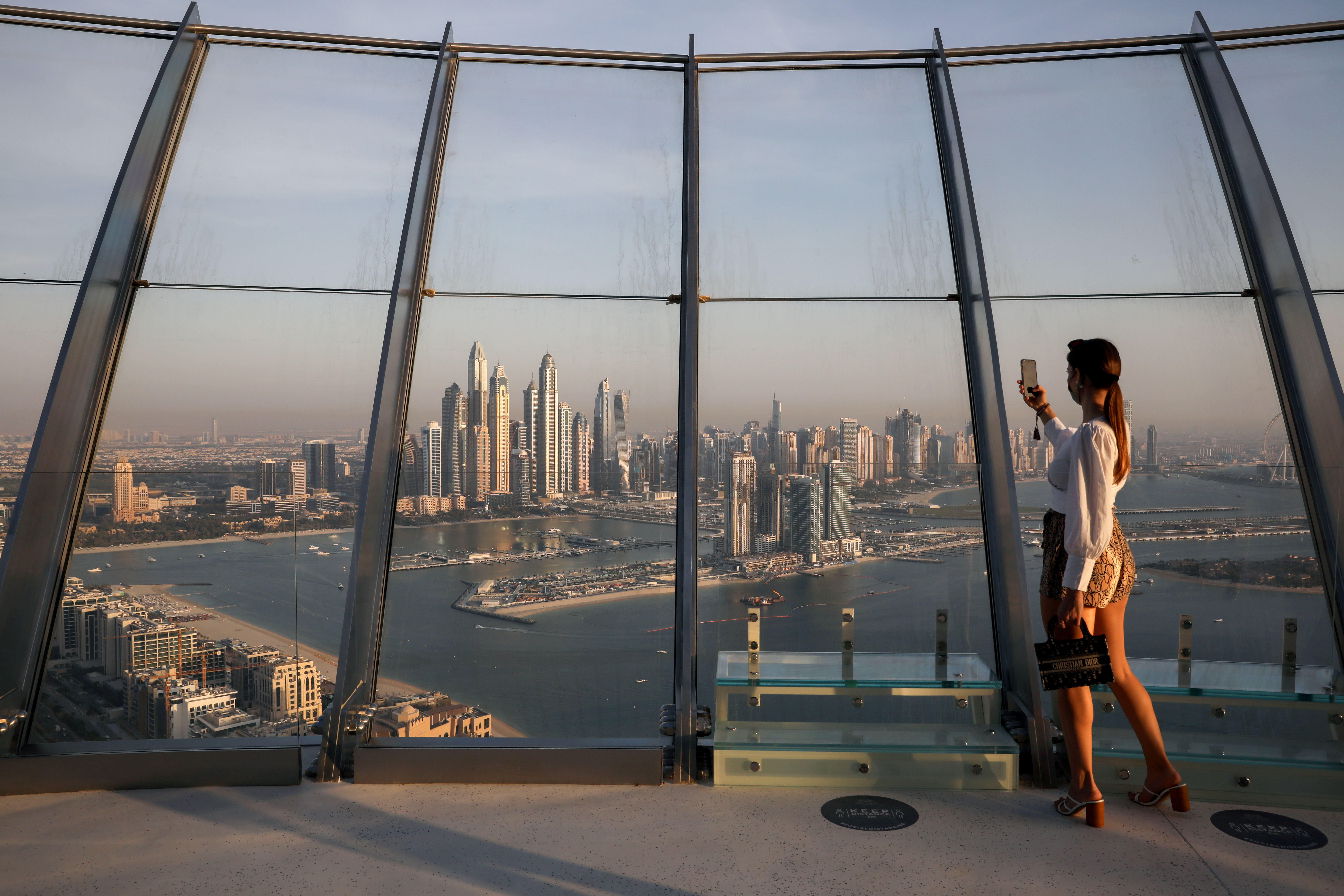 A woman takes a picture with a smartphone of the upscale Marina district from the Palm Tower in Dubai