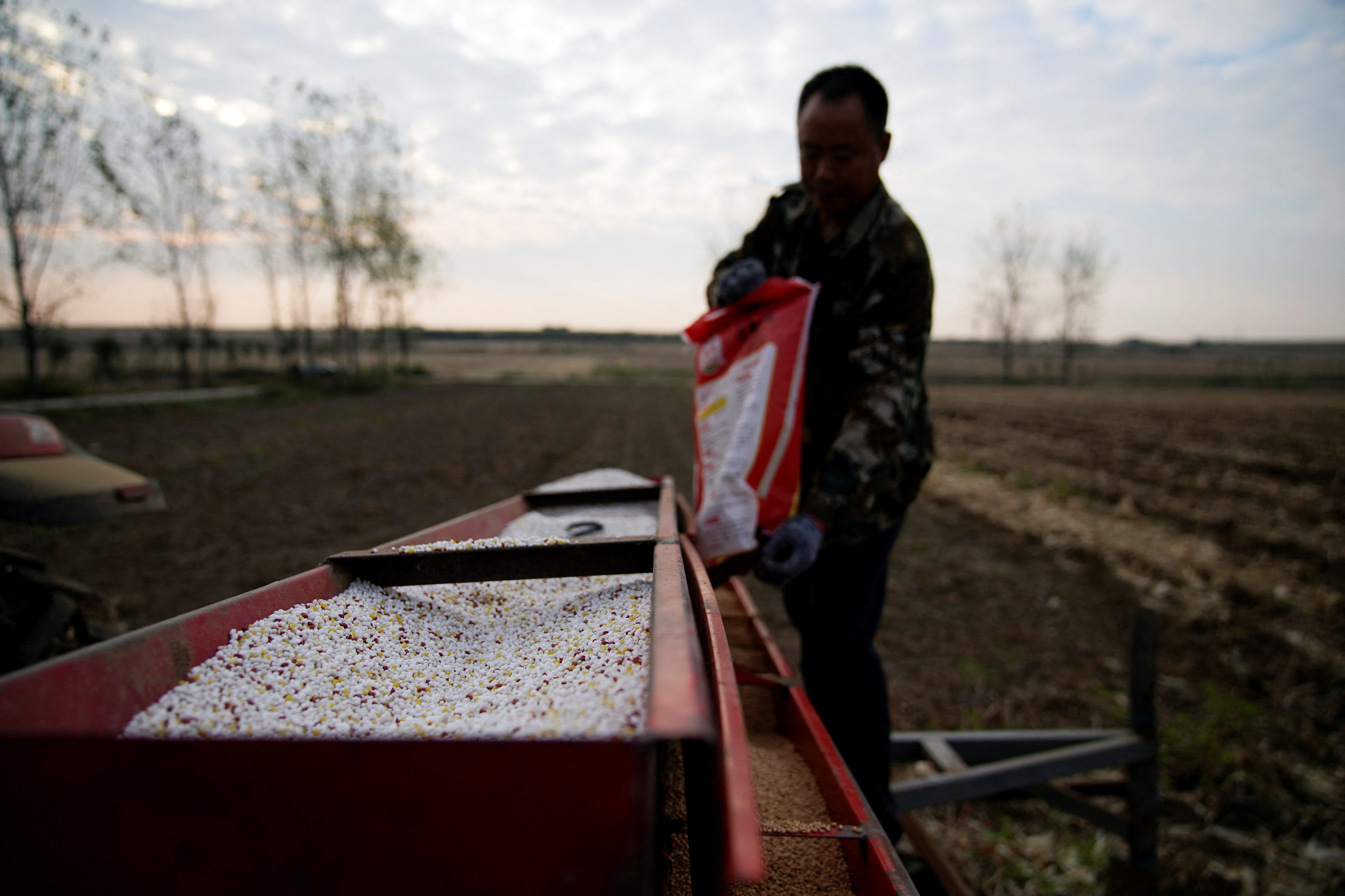 Farmer loads seeds into a seeder with fertiliser on a wheat field, in Nanyang