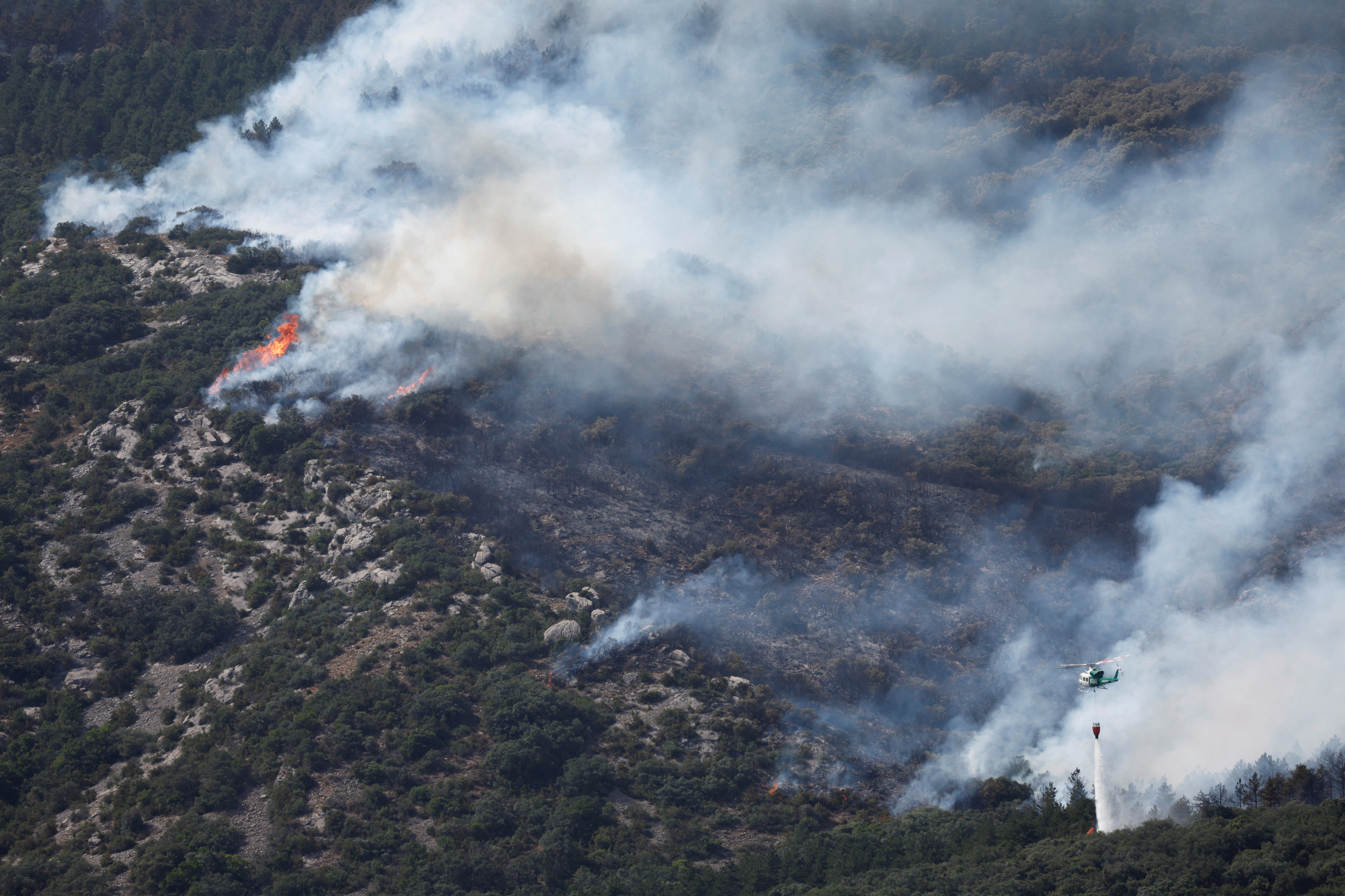Helicopter drops river water onto a forest fire, in the Sierra de Leyre mountain range