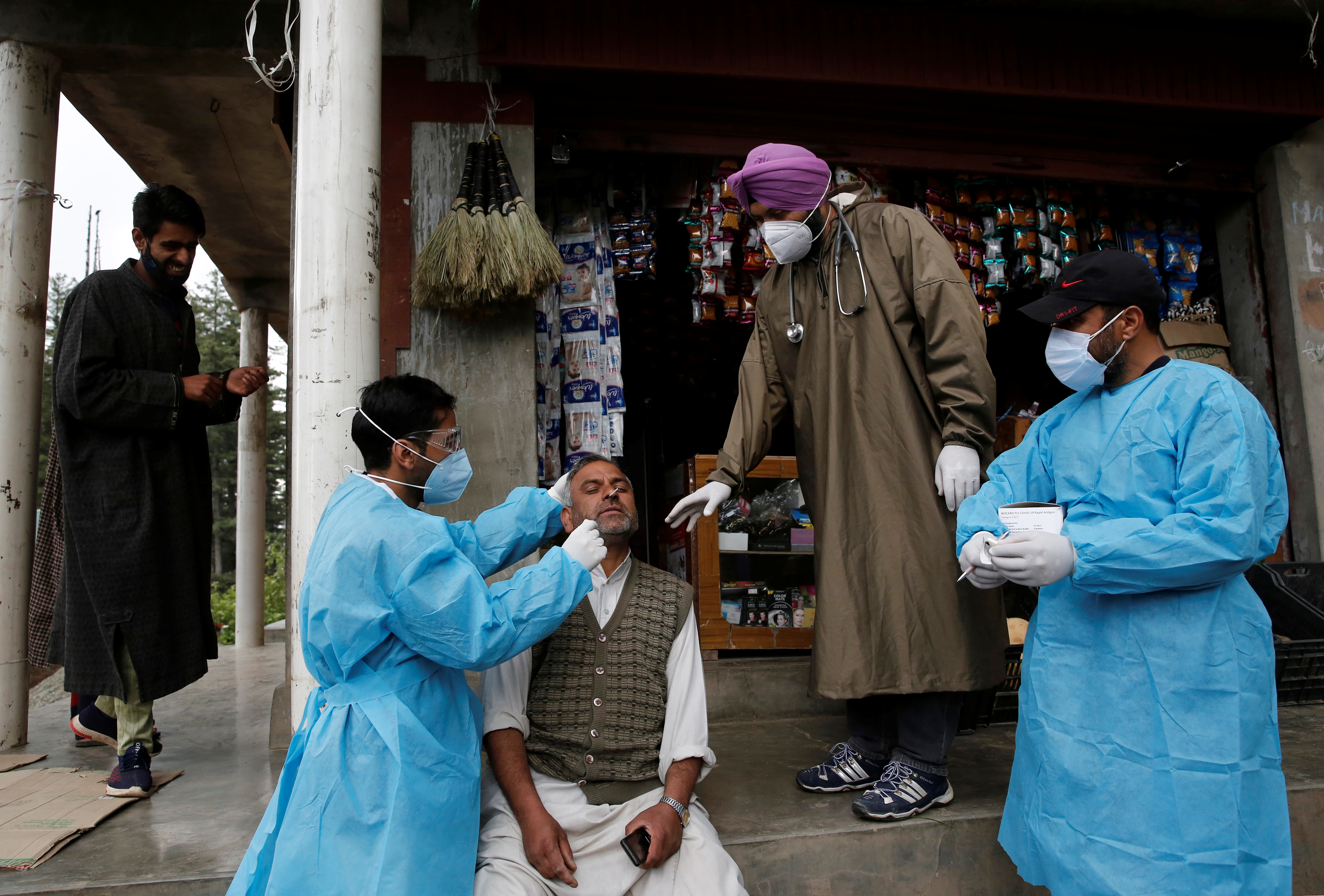 A healthcare worker takes a nasal swab sample from a man for a coronavirus disease (COVID-19) test in front of a shop in Nawroz Baba village