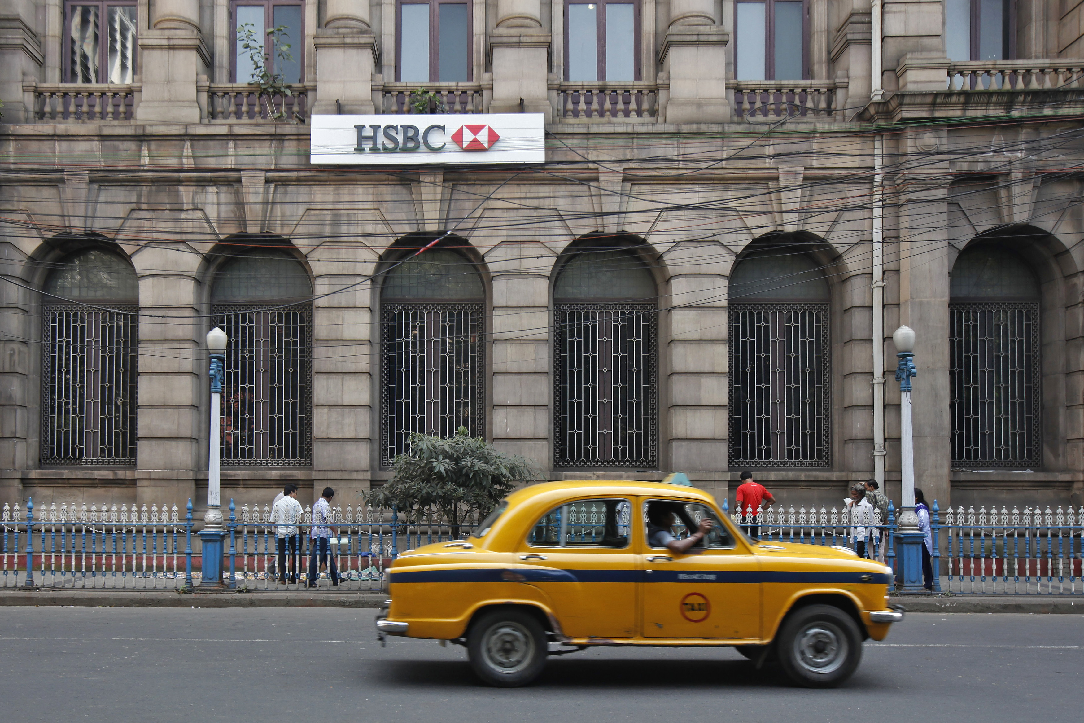 A yellow ambassador taxi drives past the HSBC bank building in Kolkata