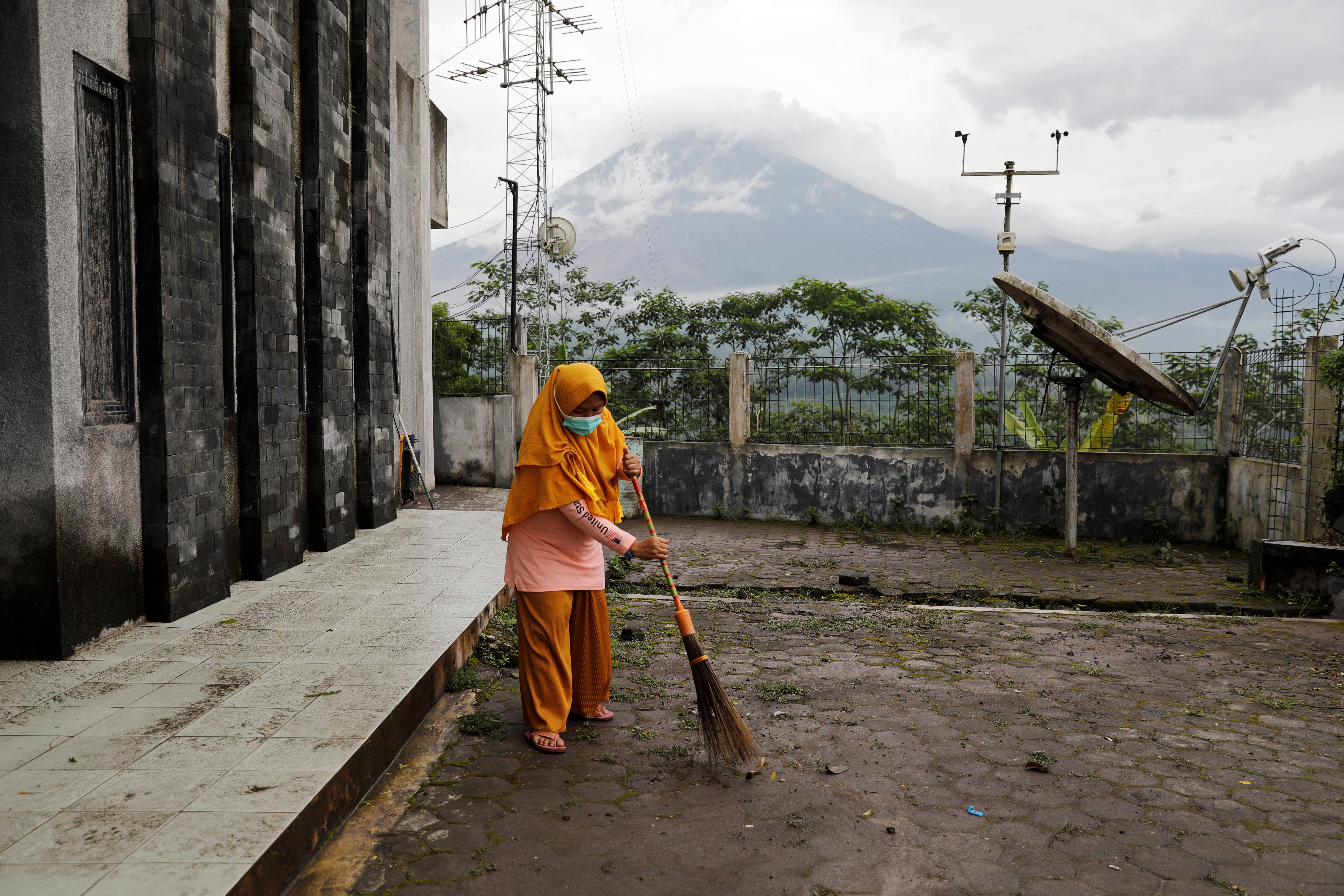 Herni, a 44-year-old local resident, sweeps ash on the ground as Mount Semeru volcano continues to spew ash and smoke, in Candipuro district, Lumajang regency, Indonesia