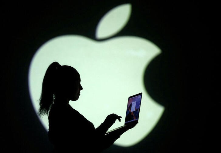 Silhouette of laptop user is seen next to a screen projection of Apple logo in this picture illustration