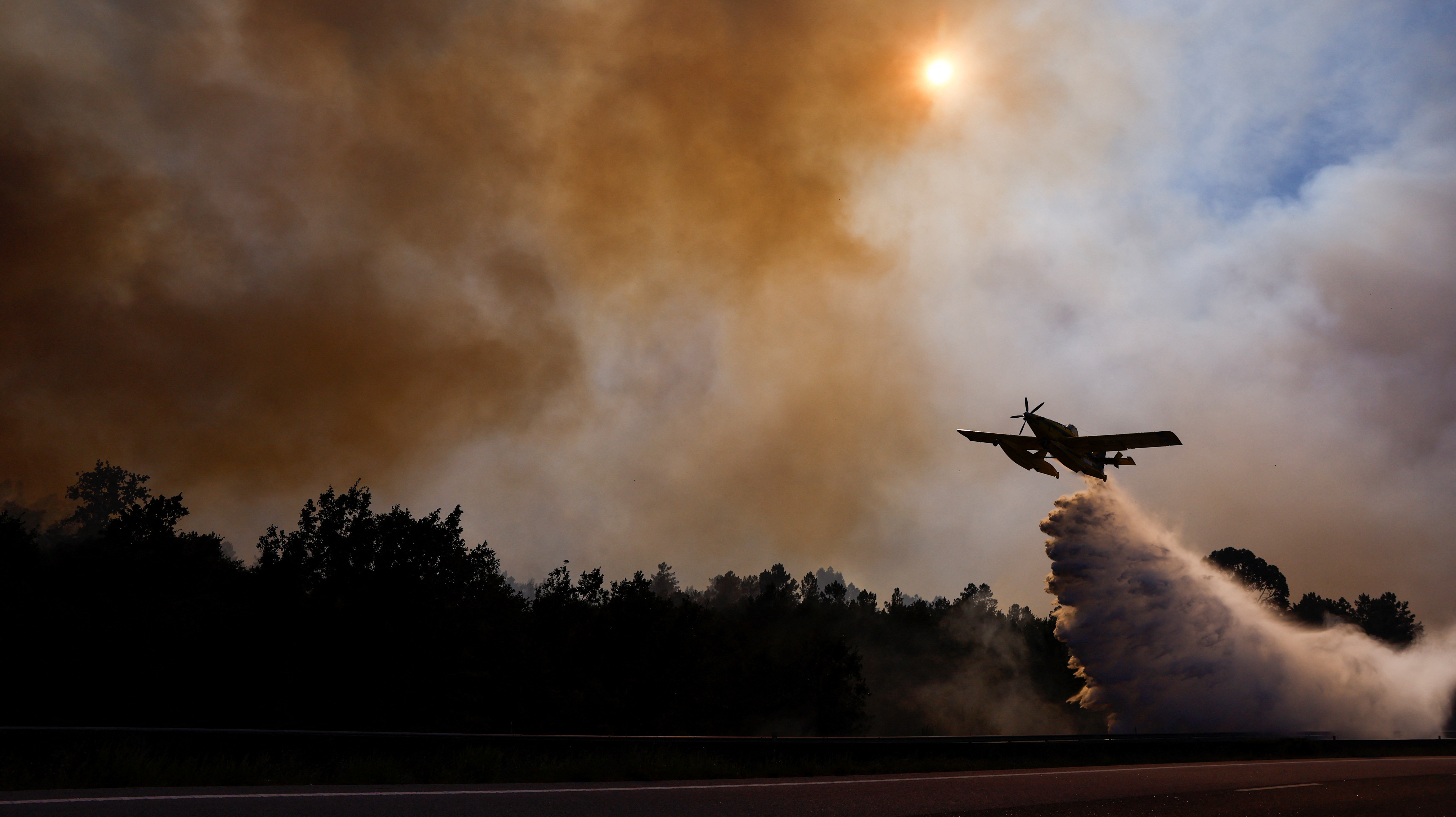 An airplane drops water on a wildfire along A25 Highway, near Freixiosa