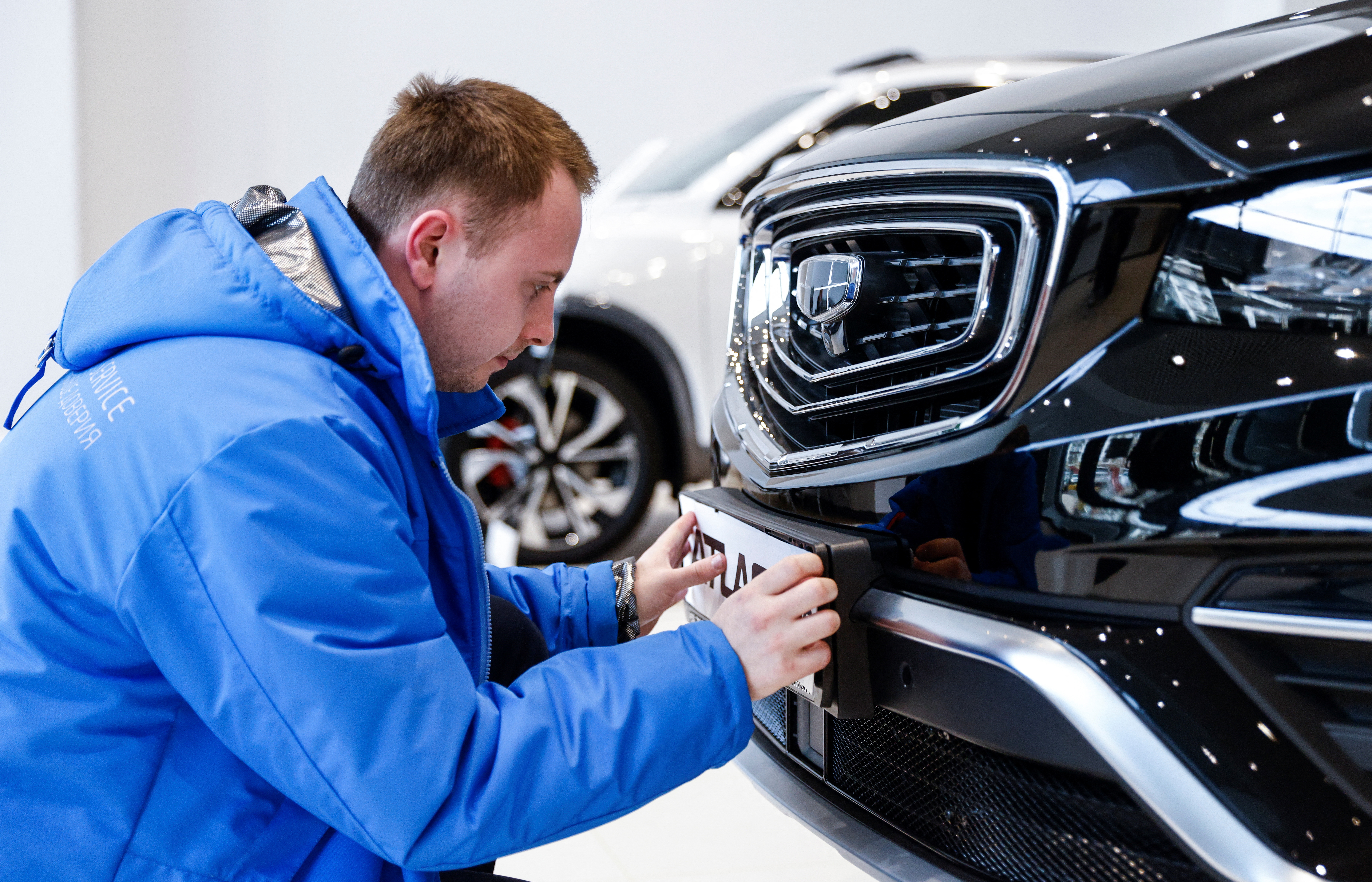 An employee attaches a brand plate to a car produced by Chinese automobile manufacturer Geely at a dealership in Moscow