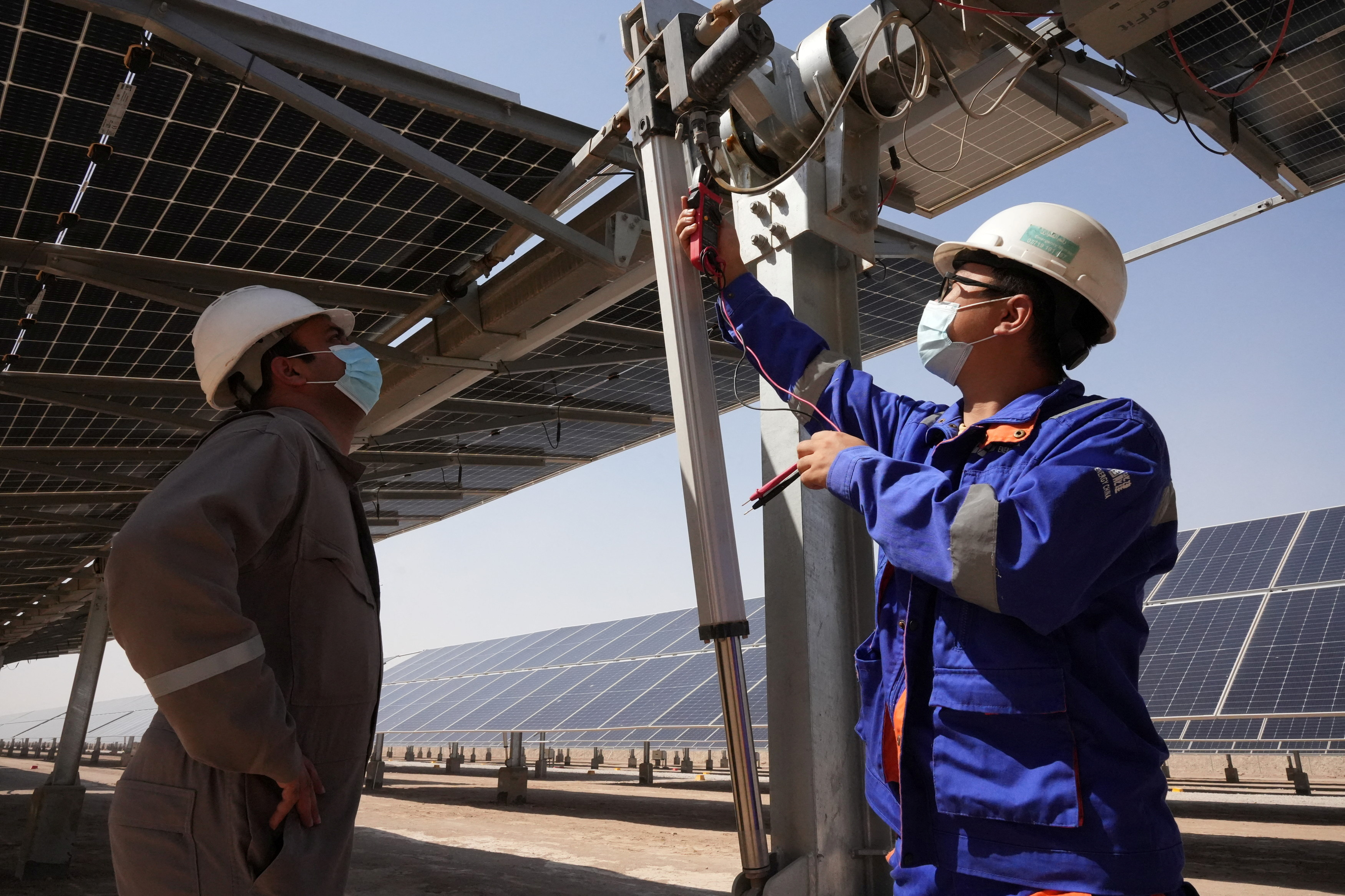 Workers check solar panels, which are a part of the solar power project at the Faihaa oil field in Basra