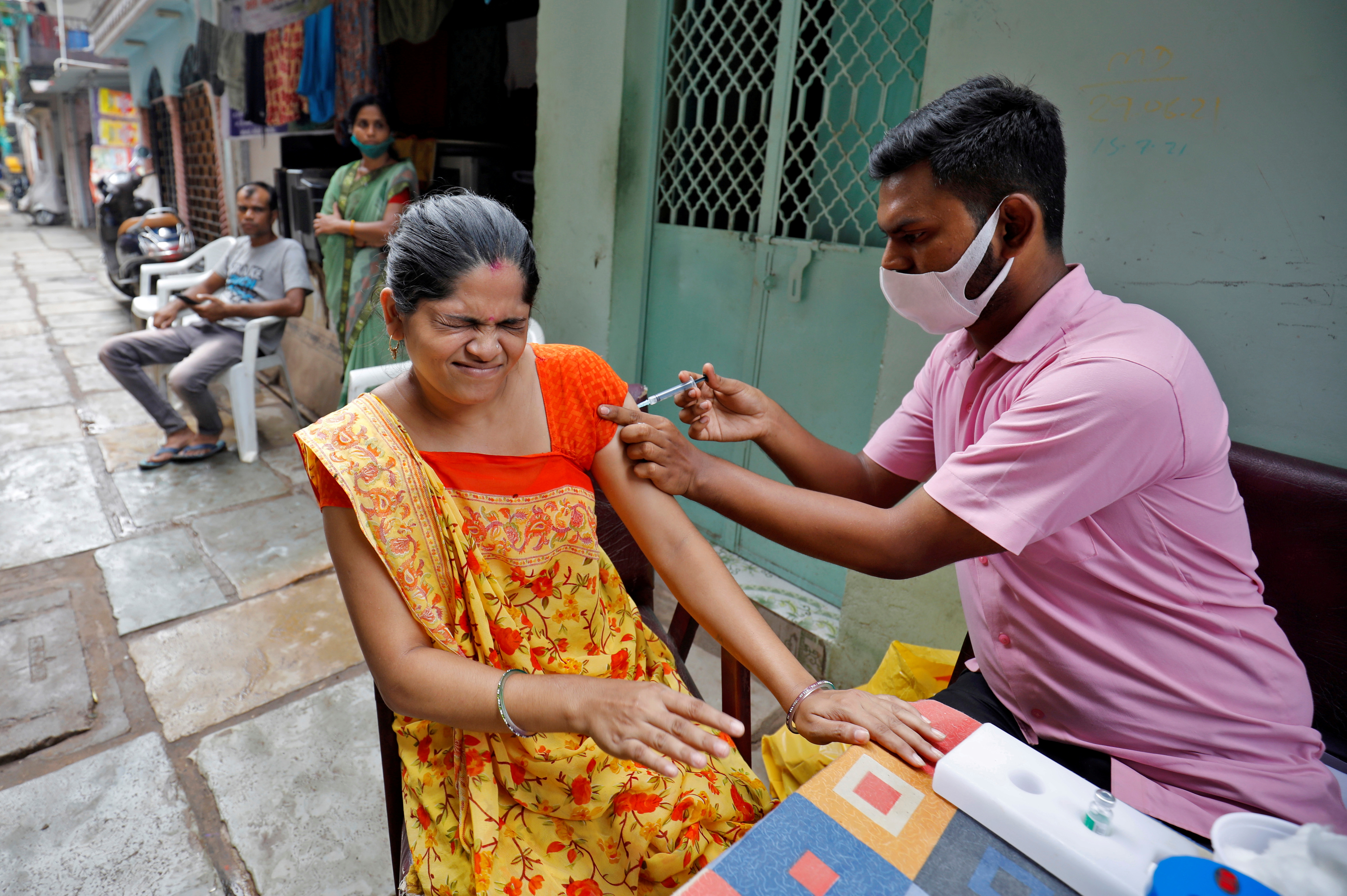 Woman reacts as she receives a dose of COVISHIELD vaccine in an alley at a slum area, in Ahmedabad