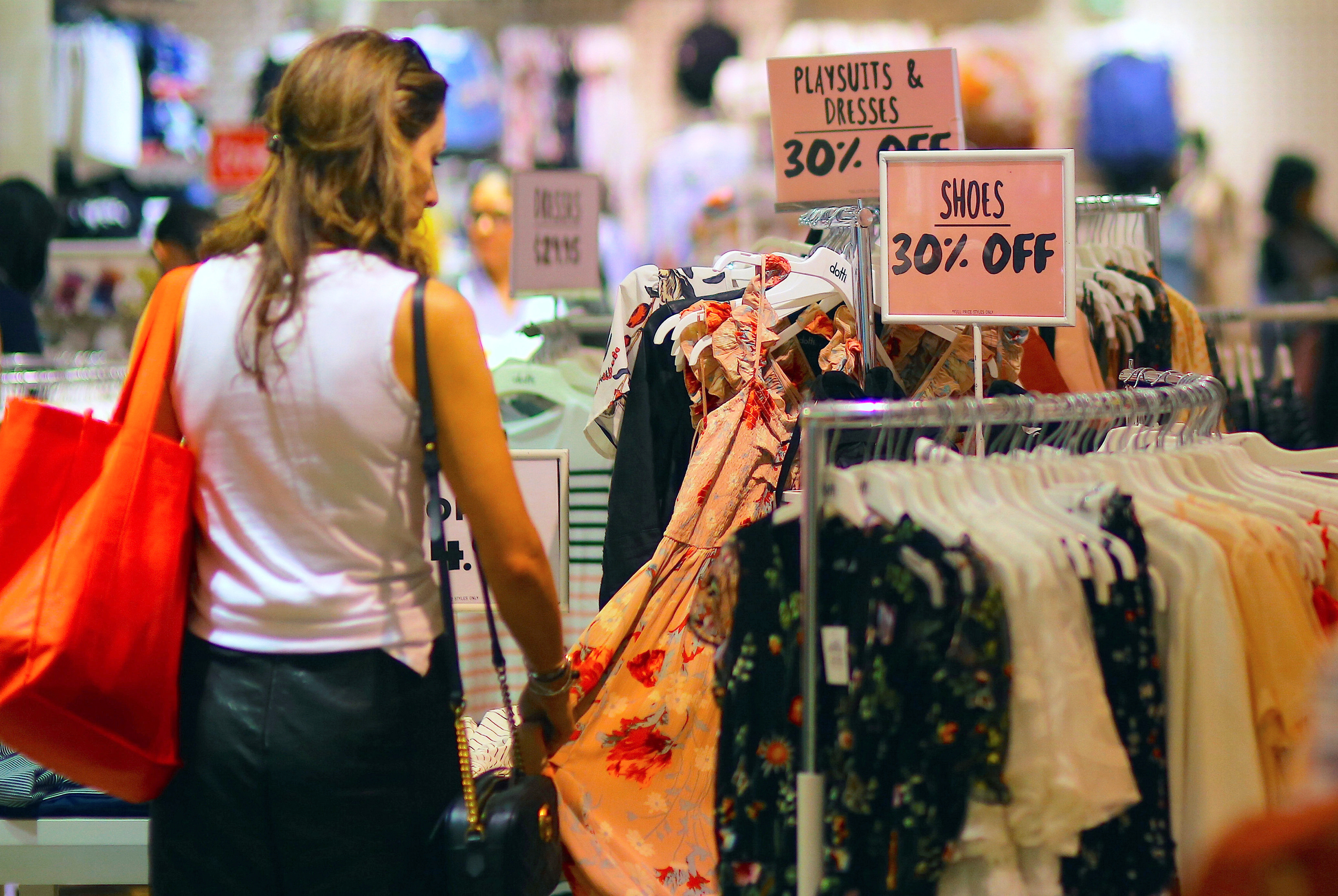 A shopper touches a dress as she inspects clothes on display next to sale signs at a retail store in central Sydney
