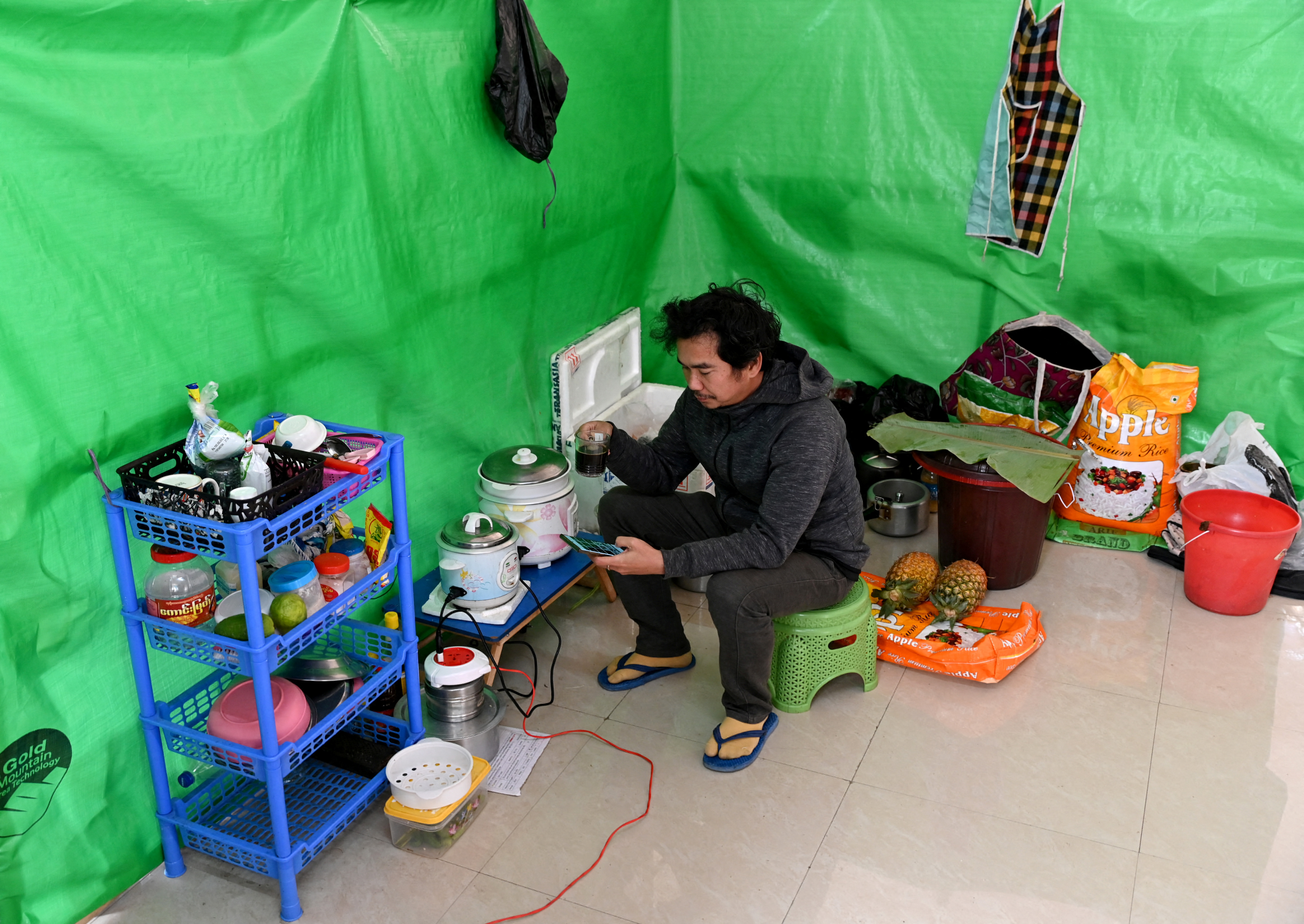 Aung Nay Myo drinks tea as he looks at a photo of his father on his phone inside a temporary shelter at an undisclosed location