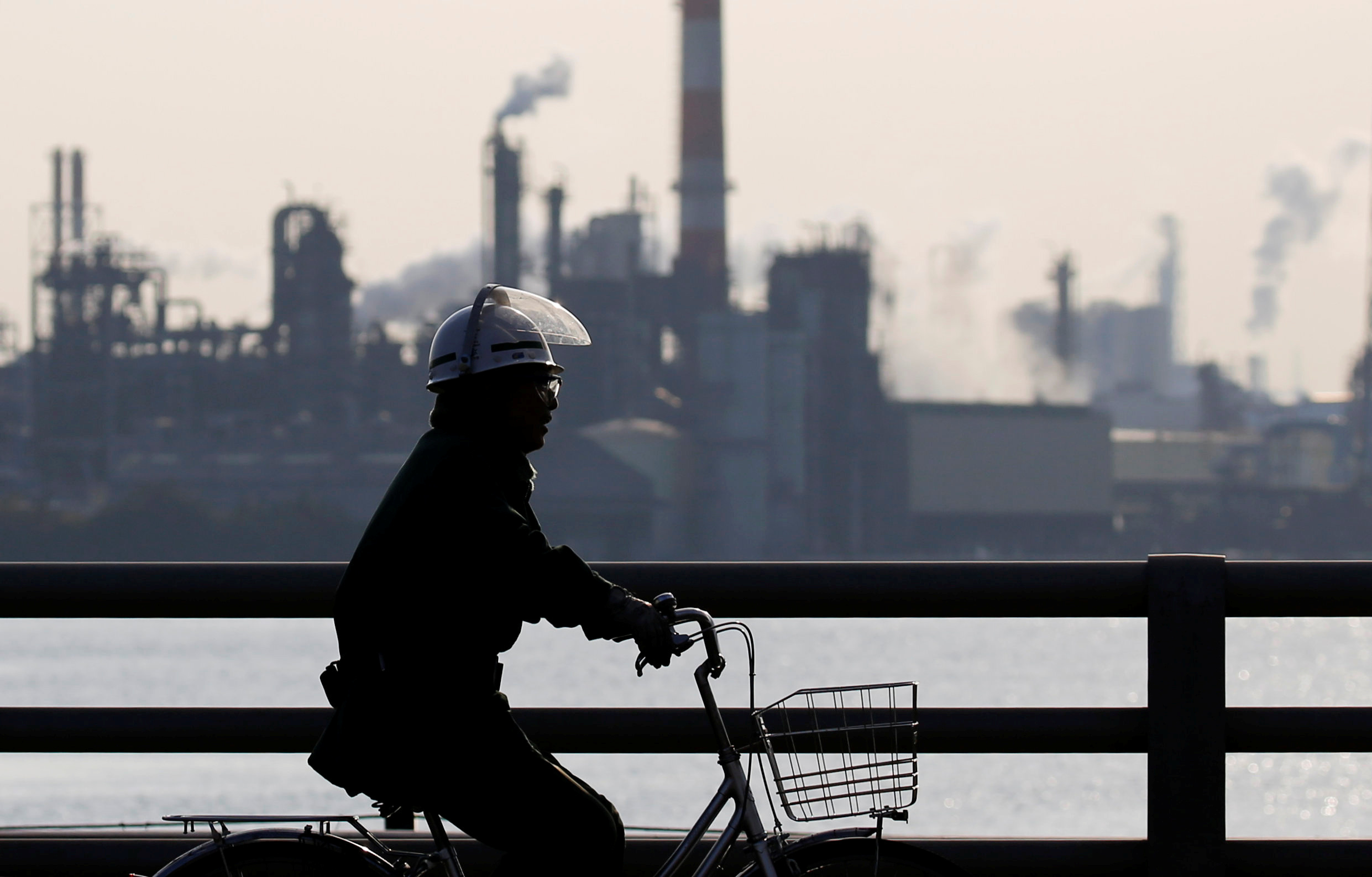A worker cycles near a factory at the Keihin industrial zone in Kawasaki, Japan