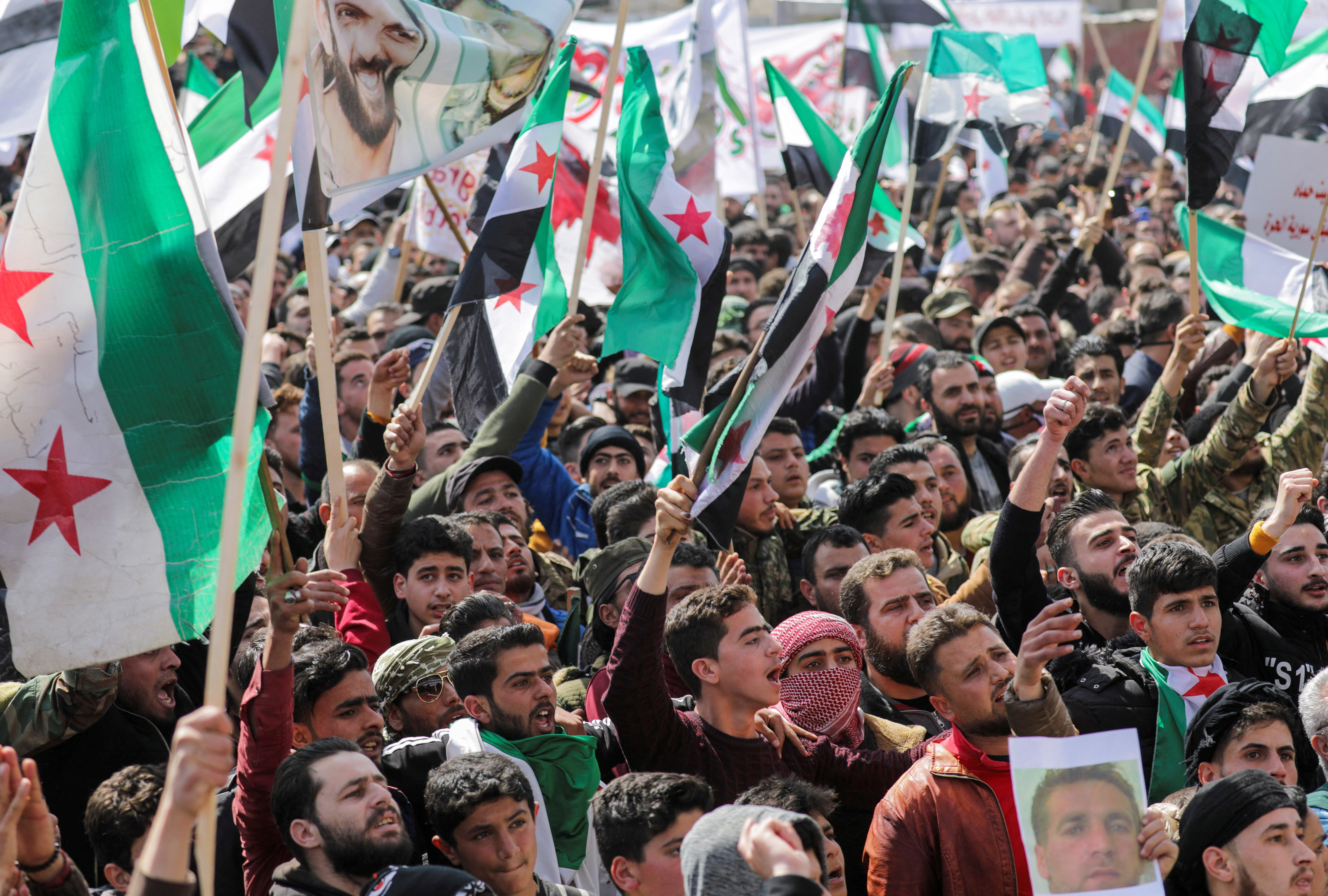 People carry banners and opposition flags during a demonstration in Idlib