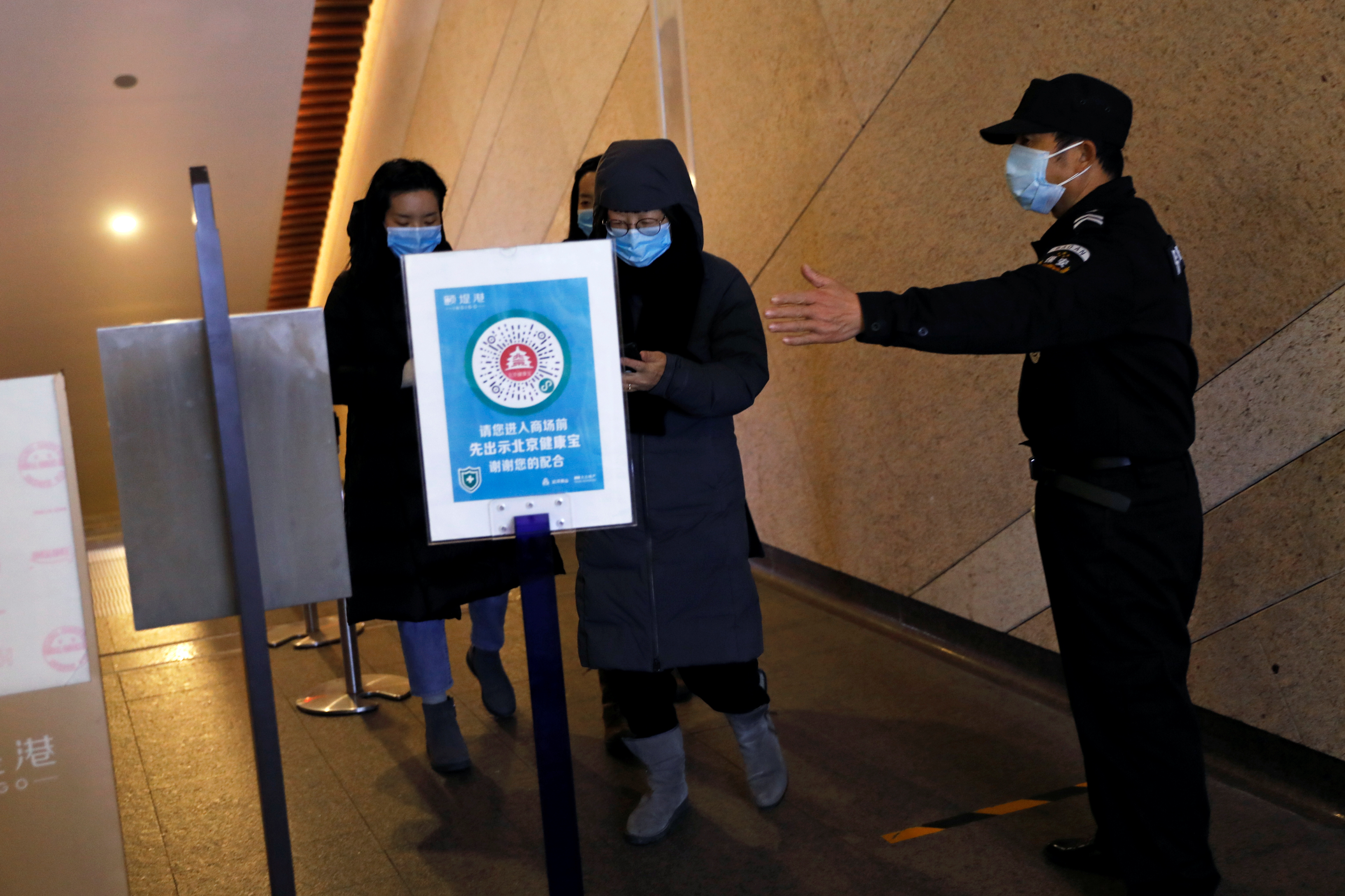 A security guard directs people to scan a QR code to track their health status before entering a shopping complex, following the new cases of the coronavirus disease (COVID-19) in Beijing