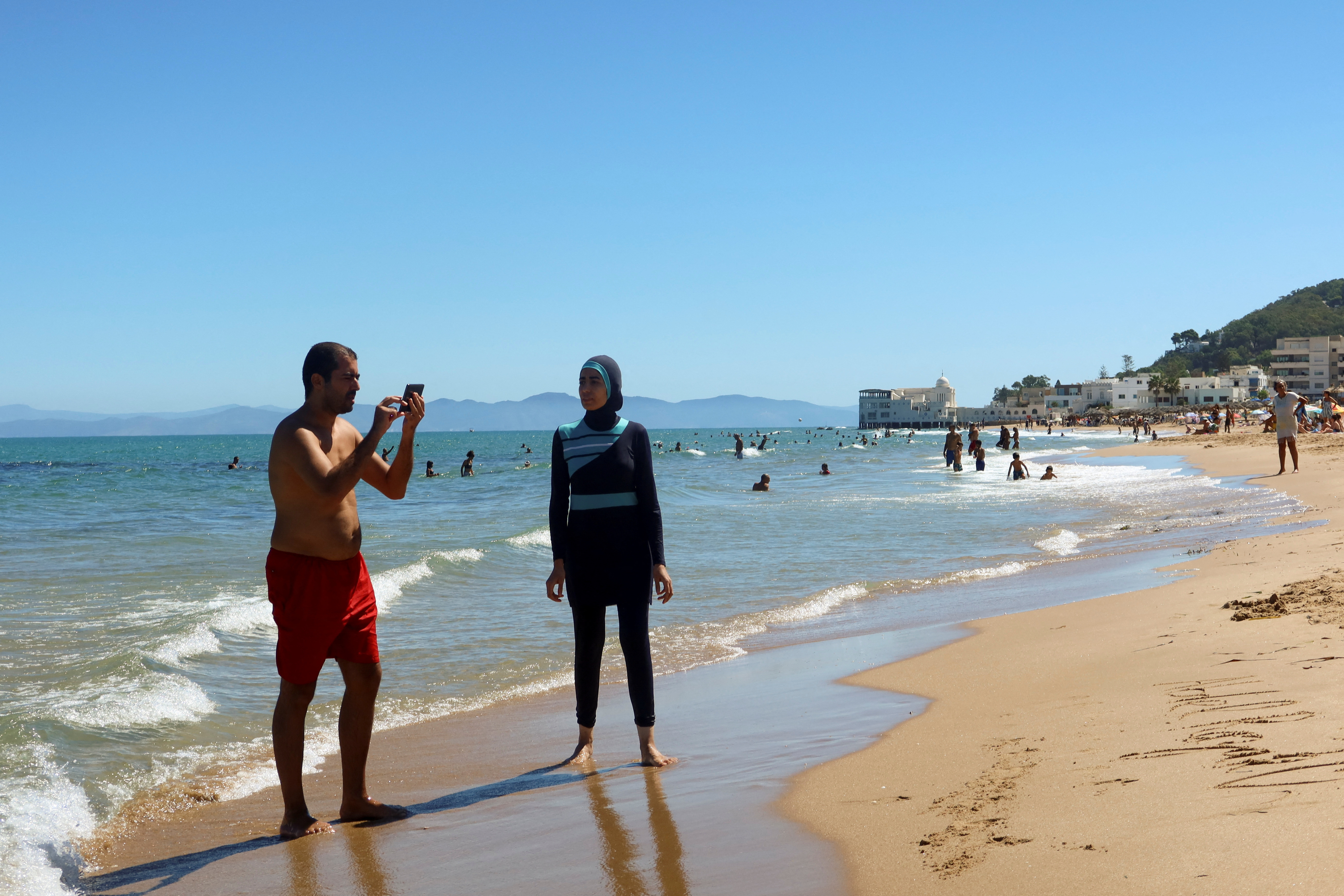 A woman, wearing a full-body burkini swimsuit, stands at La Marsa beach