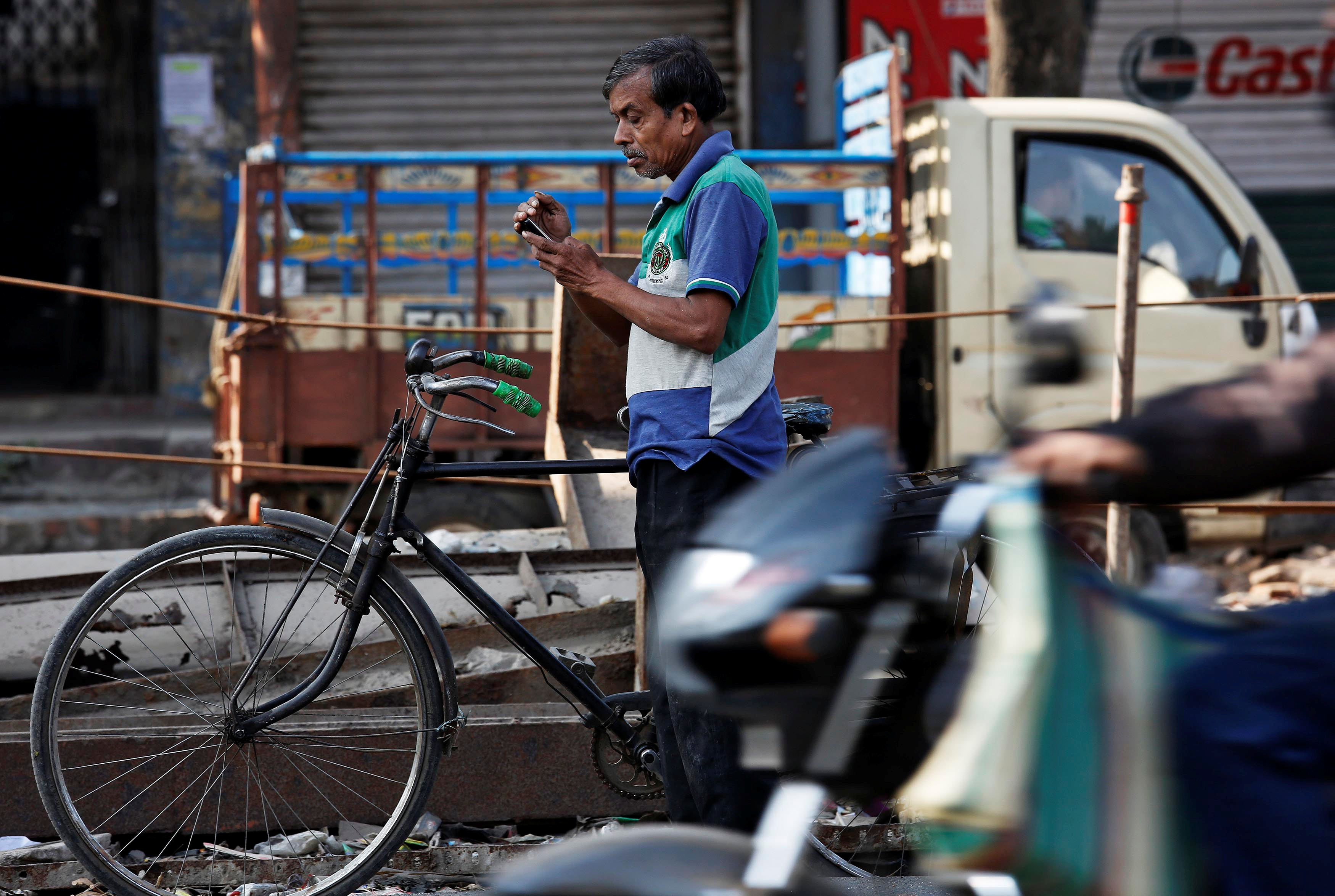 A man checks his mobile phone as he stands on a busy road in Kolkata