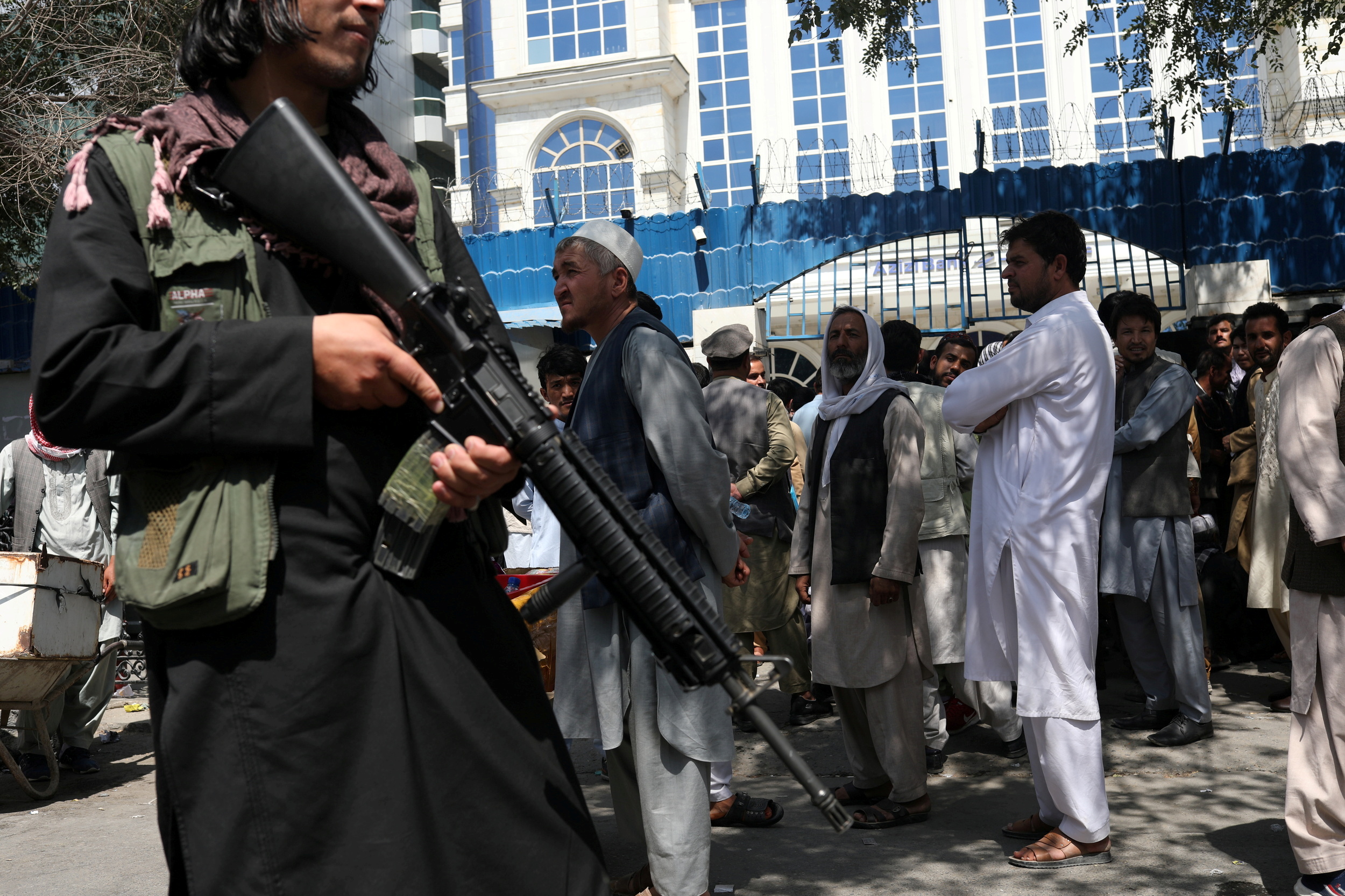 A Taliban security member holding a rifle ensures order in front of Azizi Bank in Kabul