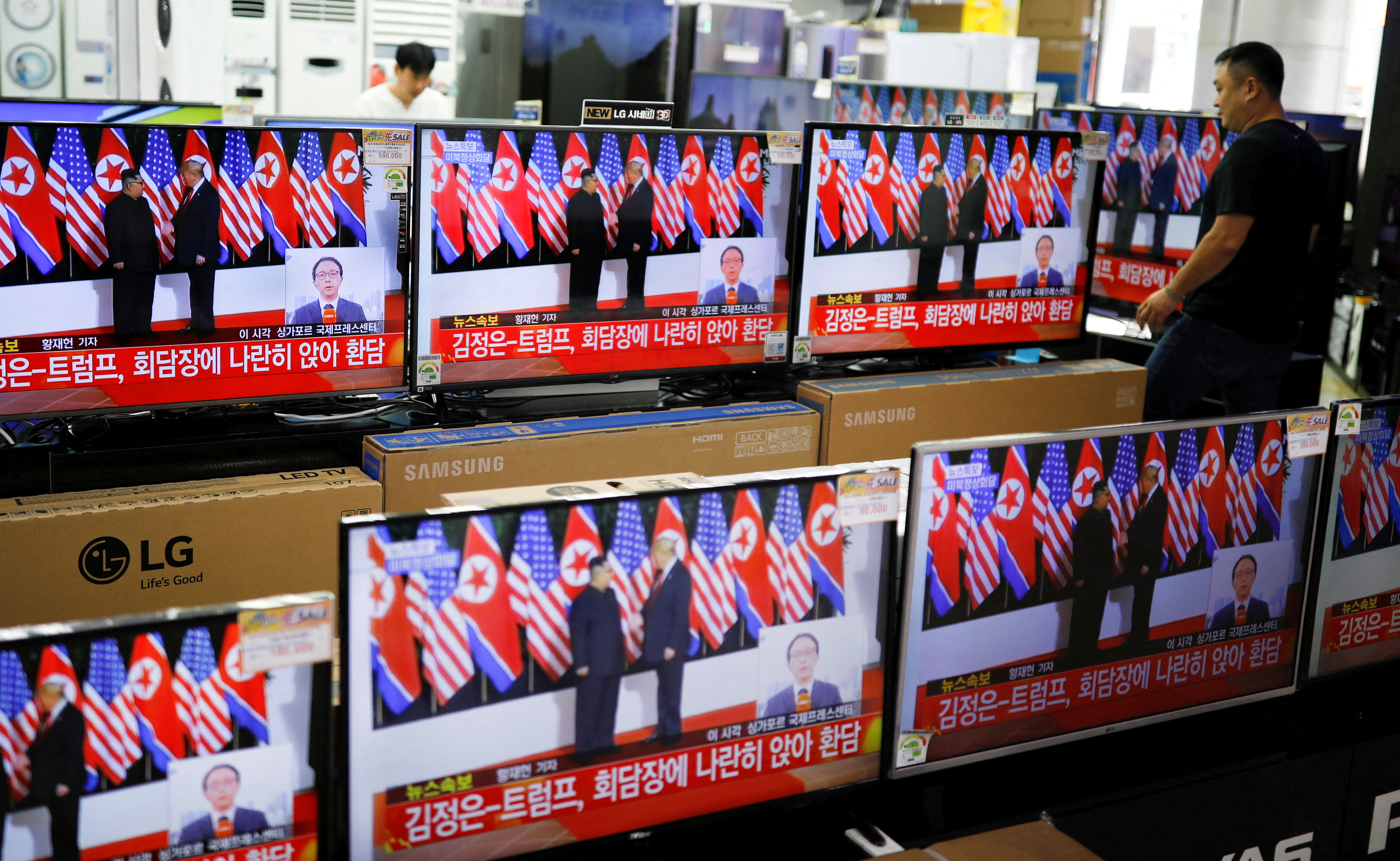 A shopkeeper walks past a set of TVs broadcasting a news report on summit between the U.S. and North Korea, in Seoul