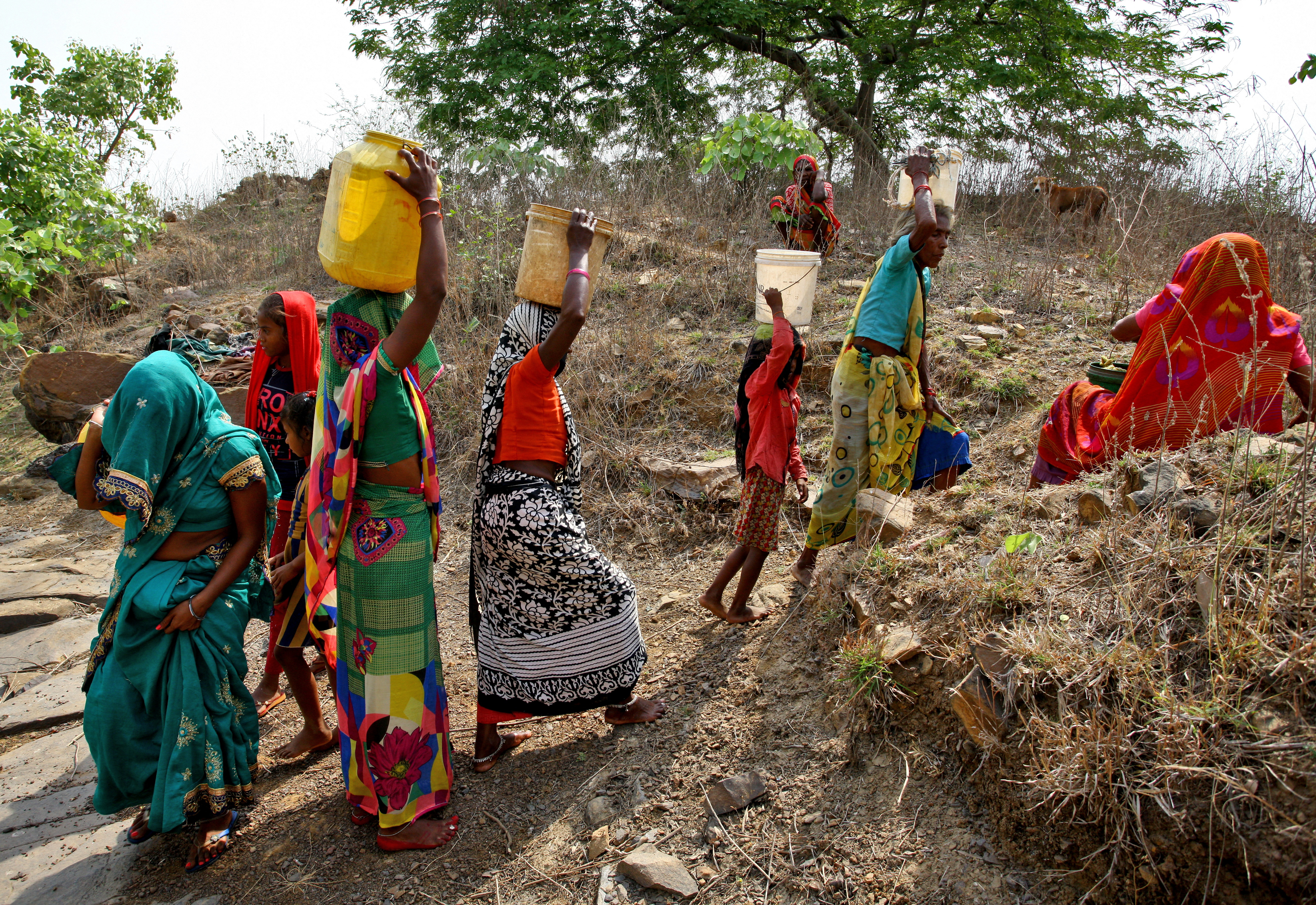 Women carry containers after filling them with water at an abandoned stone quarry on a hot day in Badama village