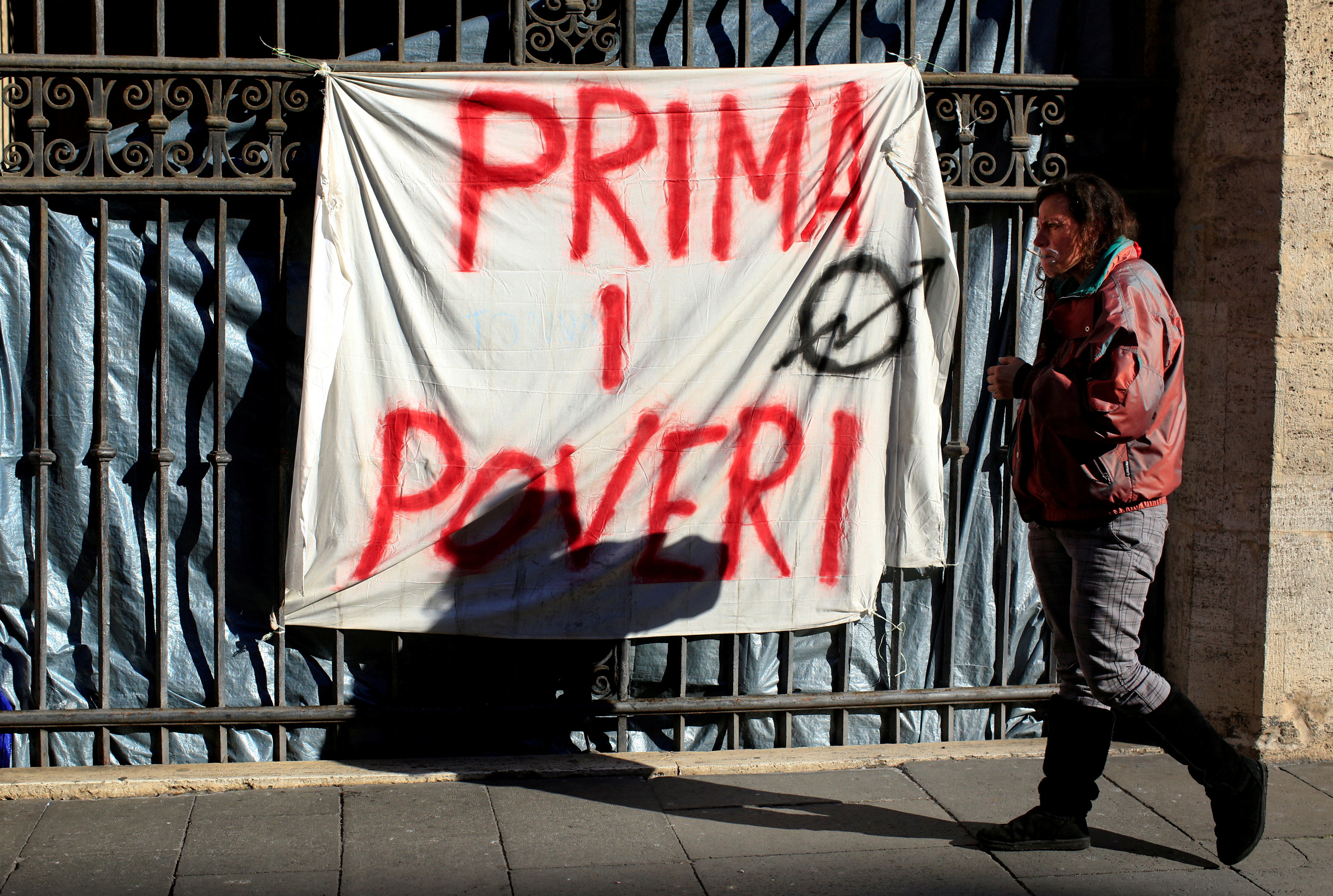 Angela Grossi walks past a banner reading "Poor first", hanging in a gate of the portico of the Basilica of the Santi Apostoli in Rome