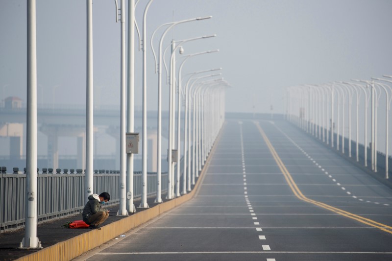 A man who arrived from Hubei province sits near a checkpoint after being refused entry at the Jiujiang Yangtze River Bridge in Jiujiang, Jiangxi province, China, as the country is hit by an outbreak of a new coronavirus, January 31, 2020. REUTERS/Thomas Peter