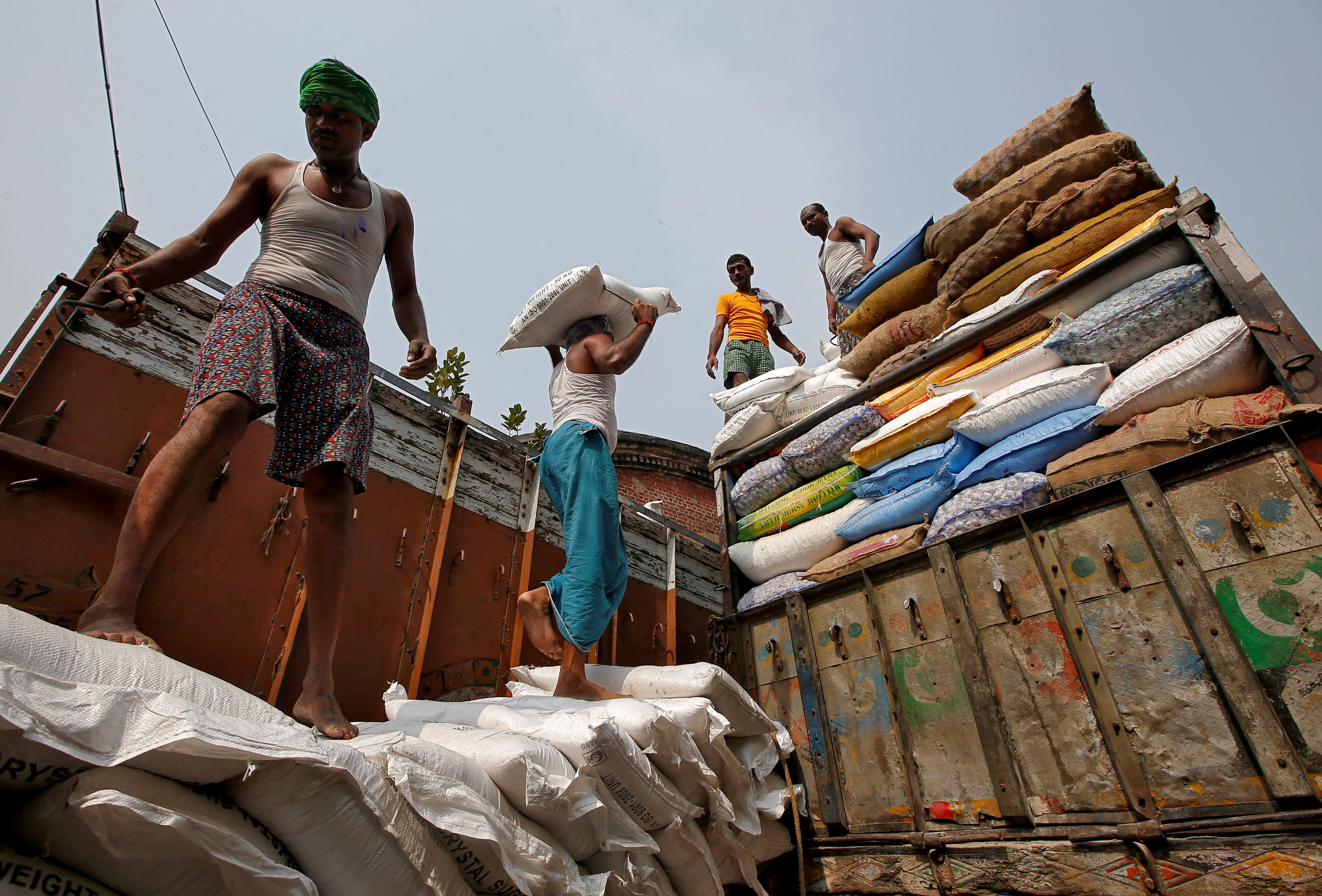 A labourer carries a sack filled with sugar to load it onto a supply truck at a wholesale market in Kolkata, India