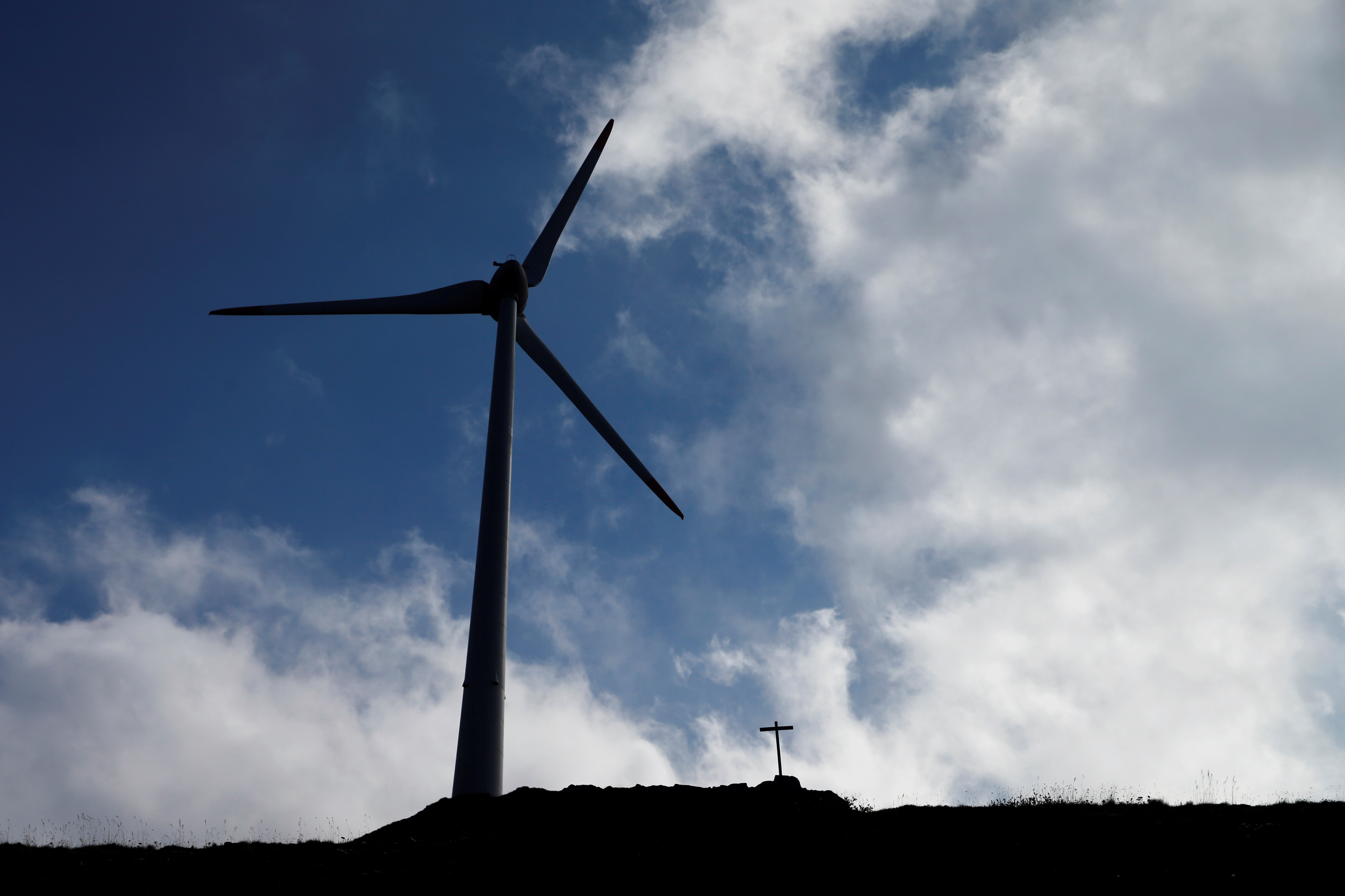 A wind turbines is pictured next to a cross at Swisswinds farm near the Nufenen Path in Gries