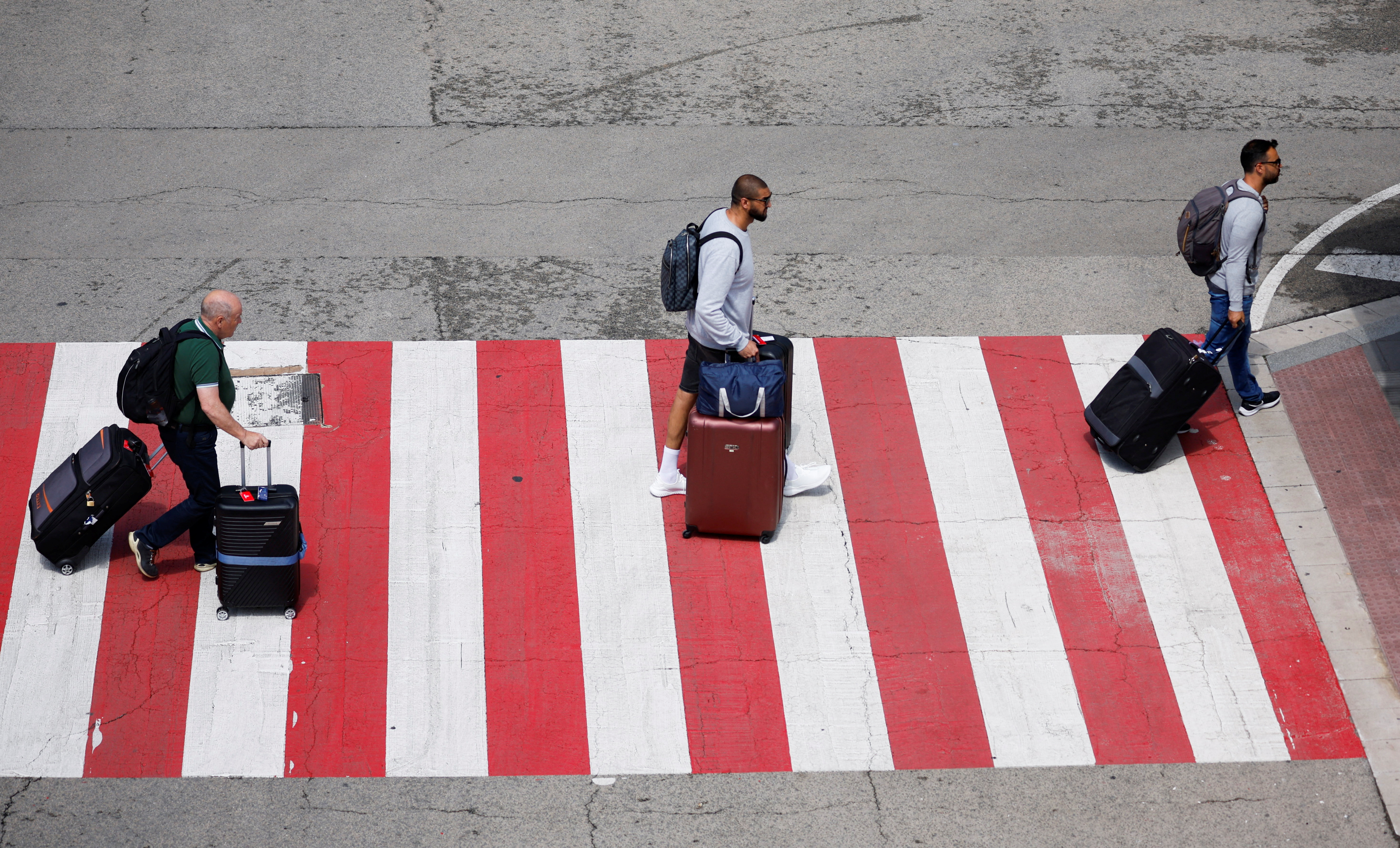 People with suitcases walk by a pedestrian crossing next to a cruise terminal at Barcelona's Port