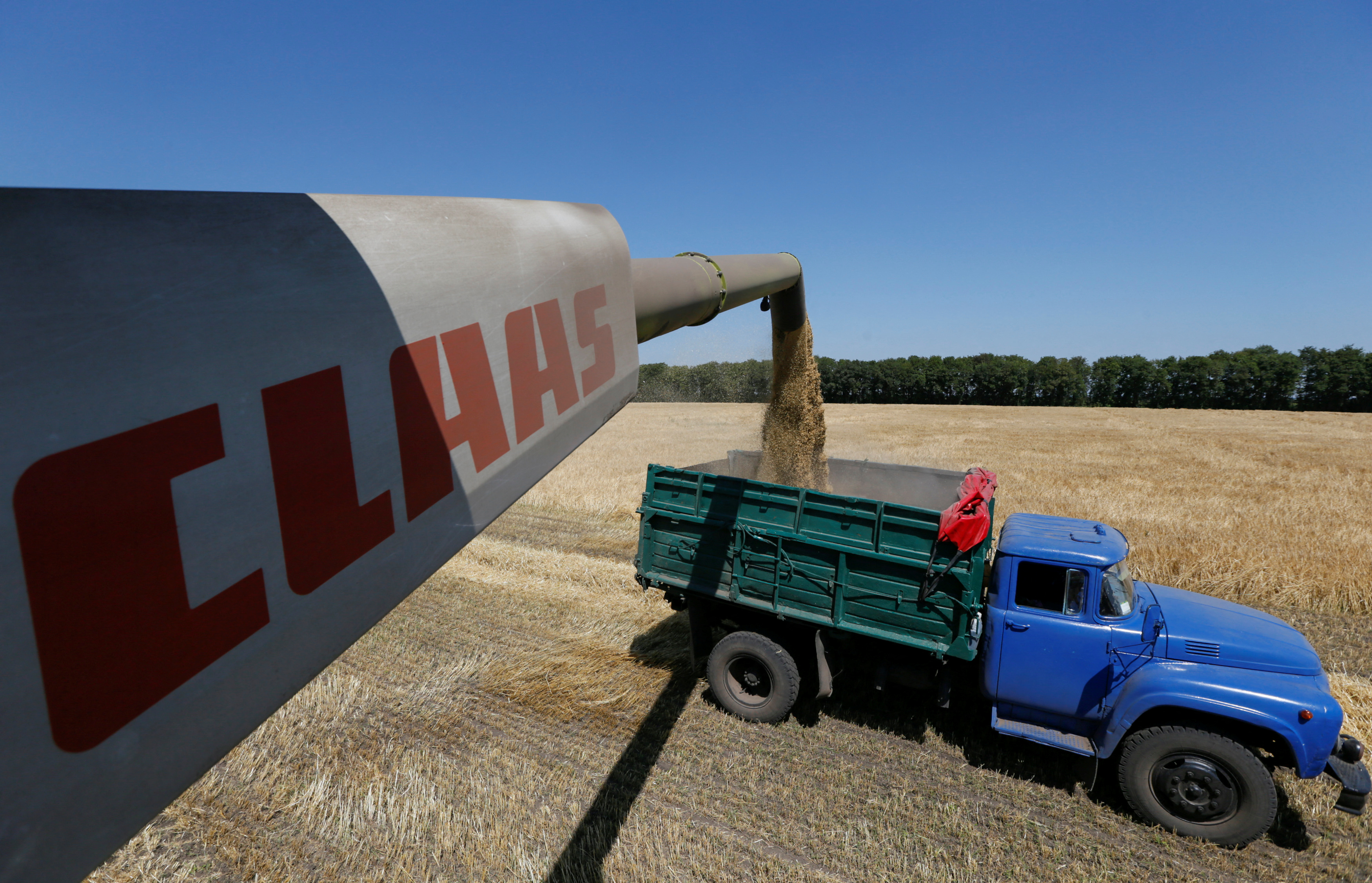 Combine harvester loads truck with barley in field in Kiev region