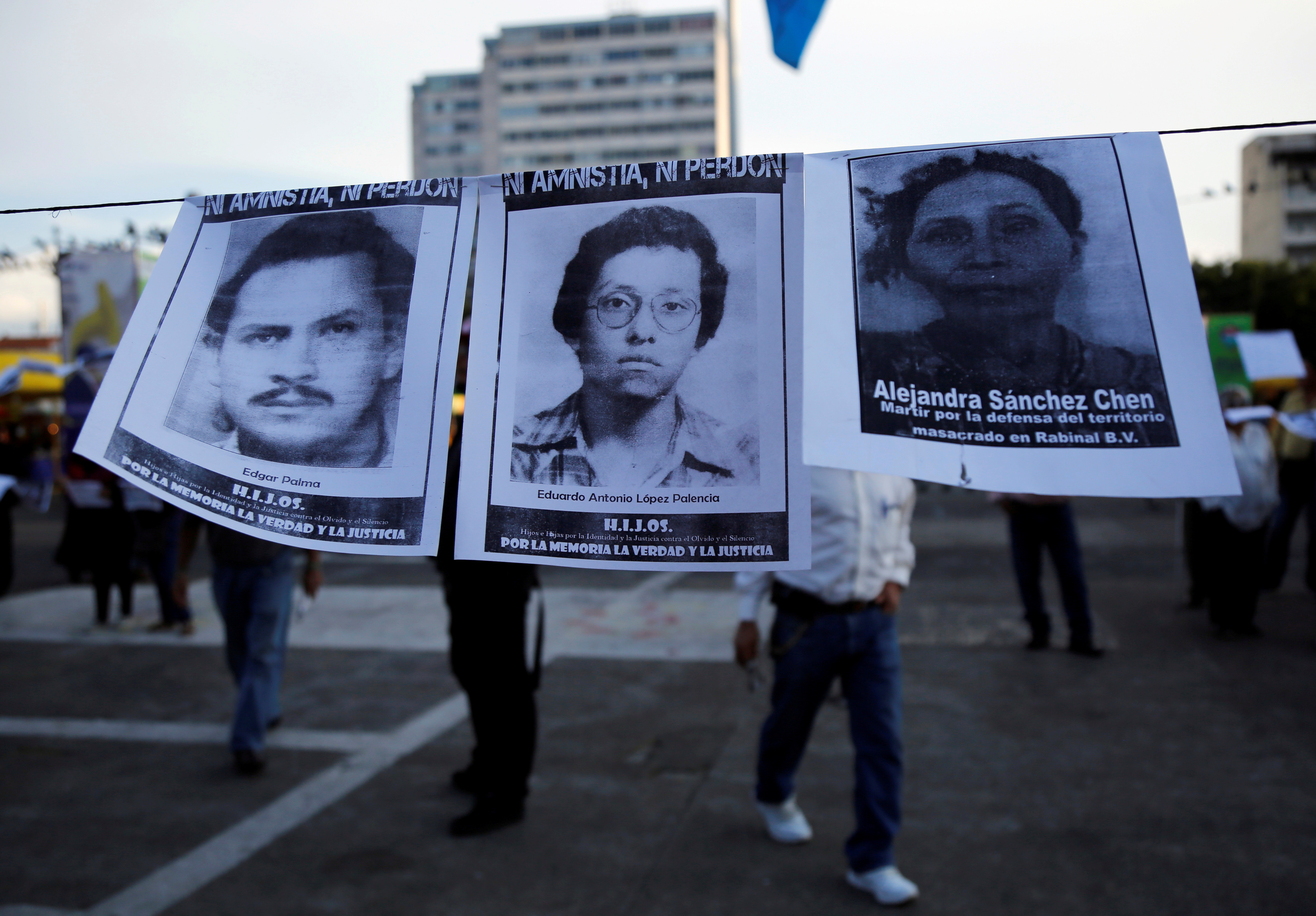 People walk past pictures of people who disappeared during Guatemala's civil war at an demonstration against the former Guatemalan military dictator Efrain Rios Montt, who died on Sunday at aged 91, in Guatemala City
