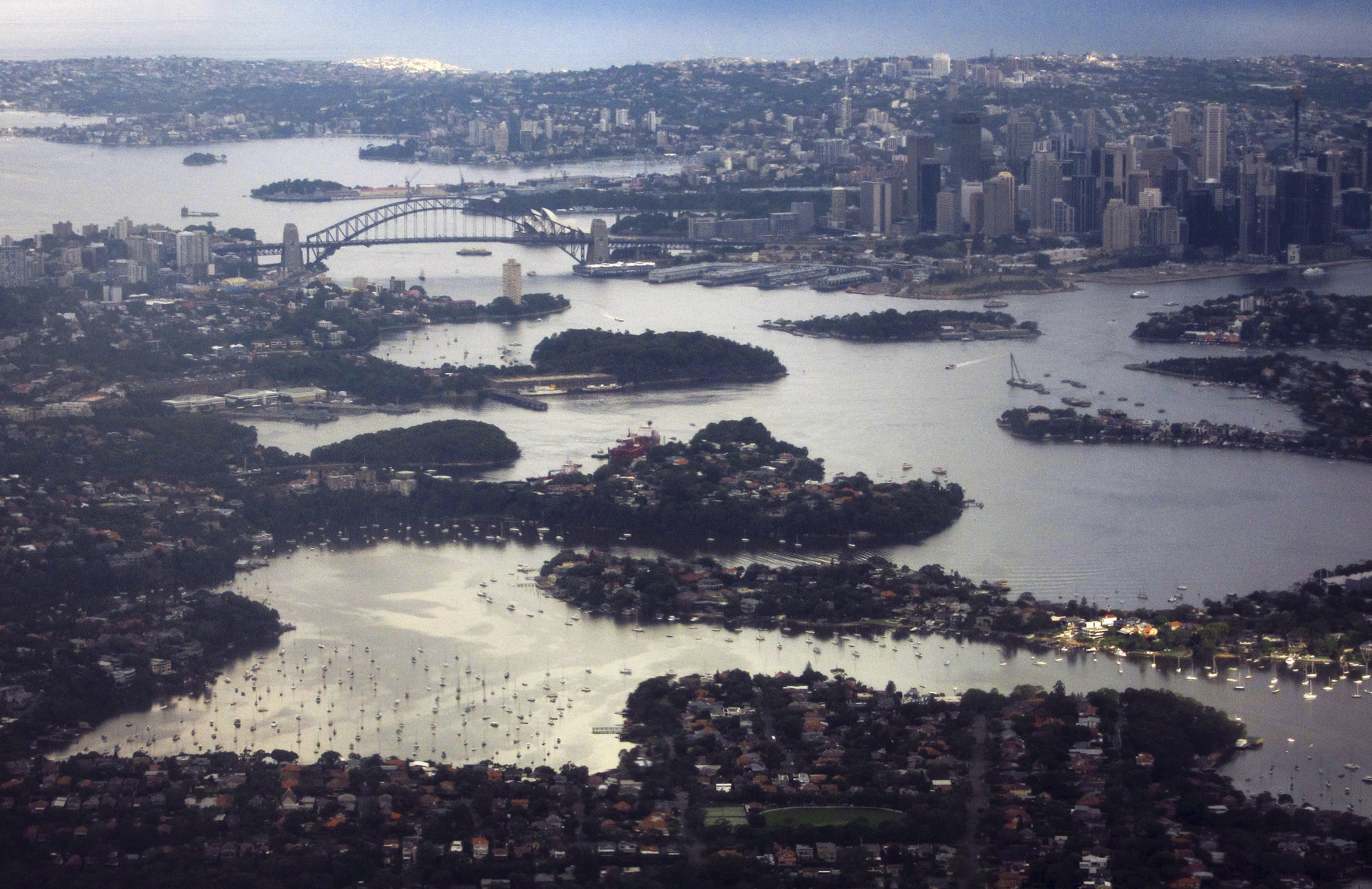 Aerial picture shows Sydney Harbour Bridge and Central Business District behind houses along the foreshore of Sydney Harbour