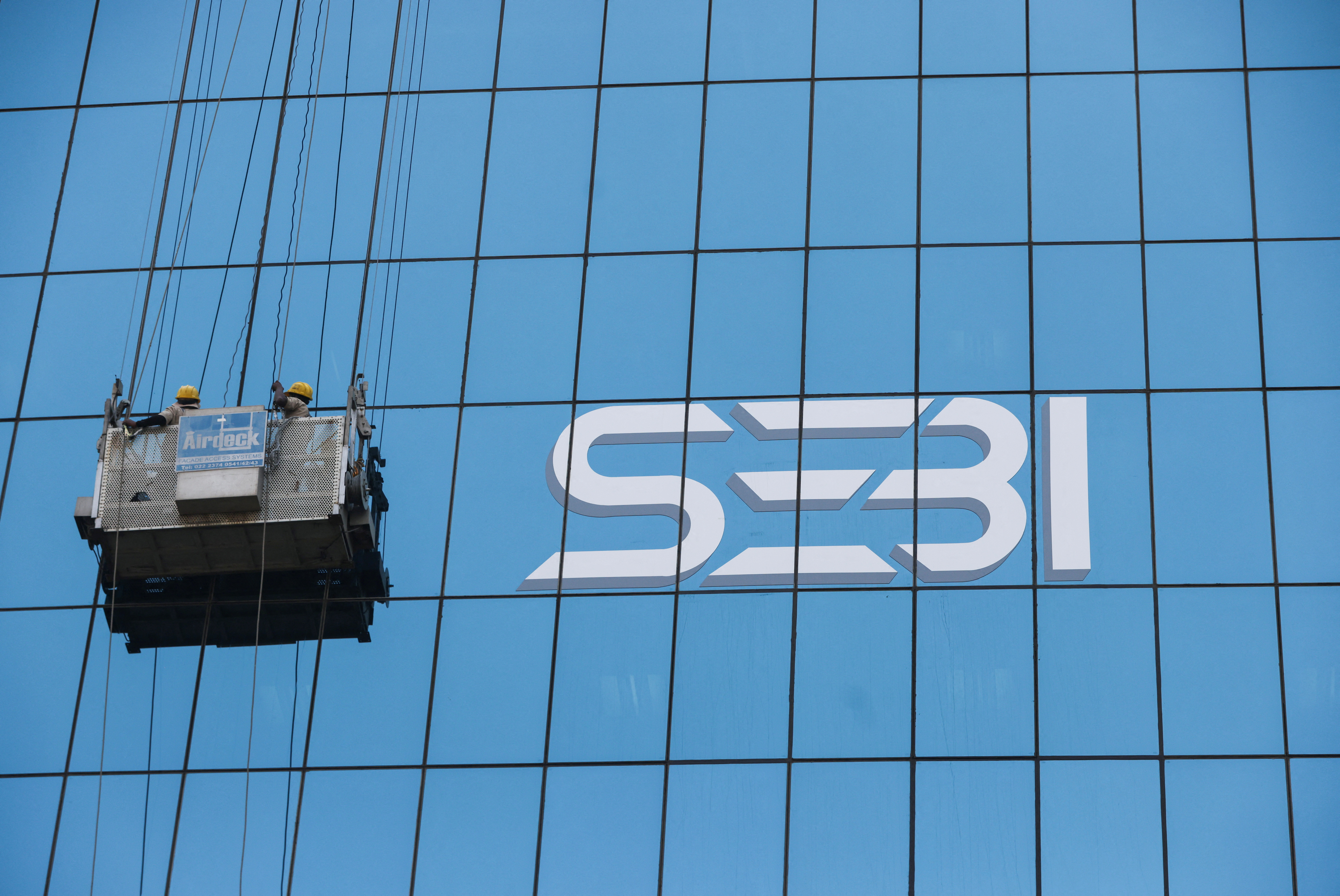 Window cleaners work next to the new logo of the Securities and Exchange Board of India (SEBI) at its headquarters in Mumbai