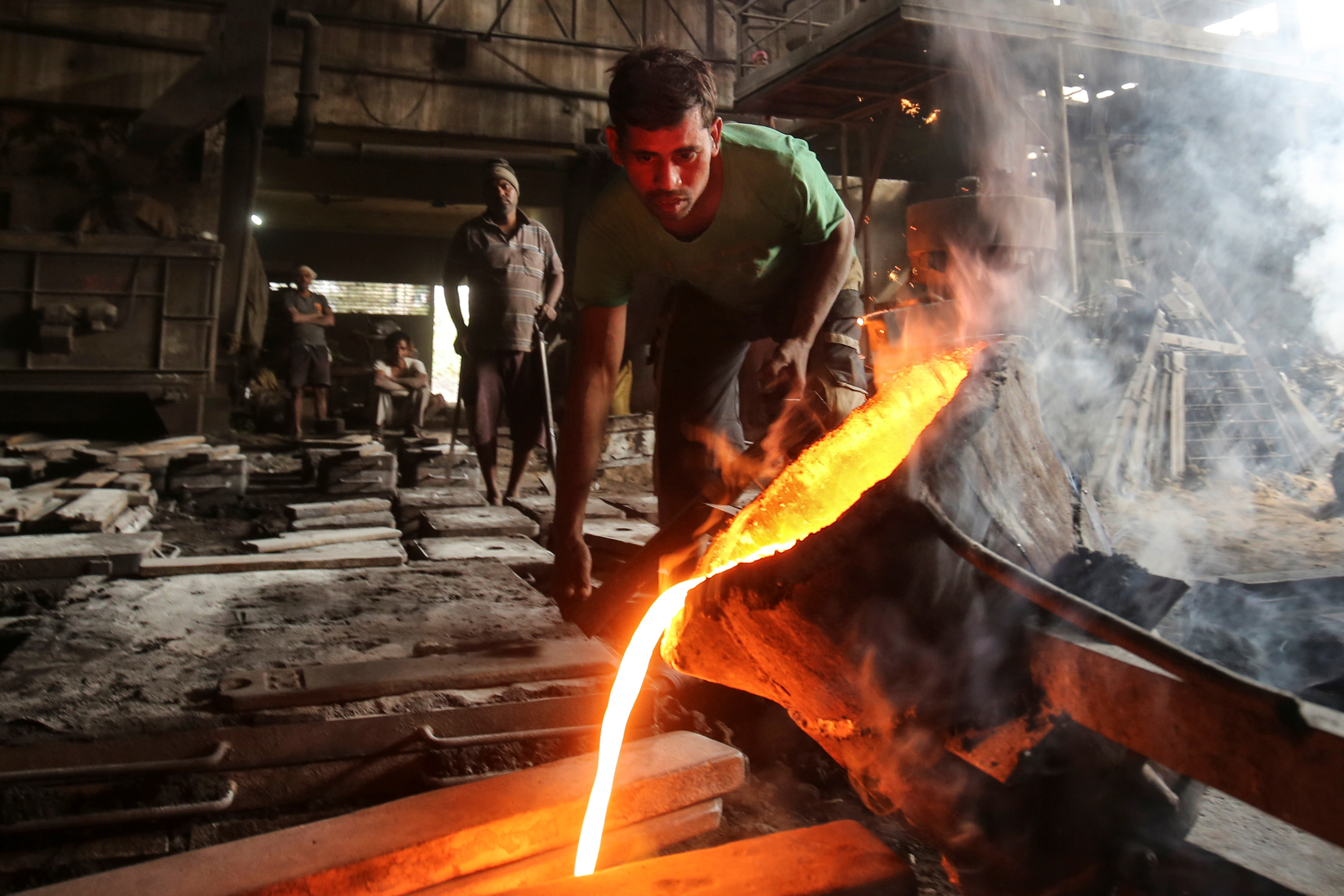 A worker pours molten iron from a ladle to make automobile spare parts inside an iron casting factory in Ahmedabad