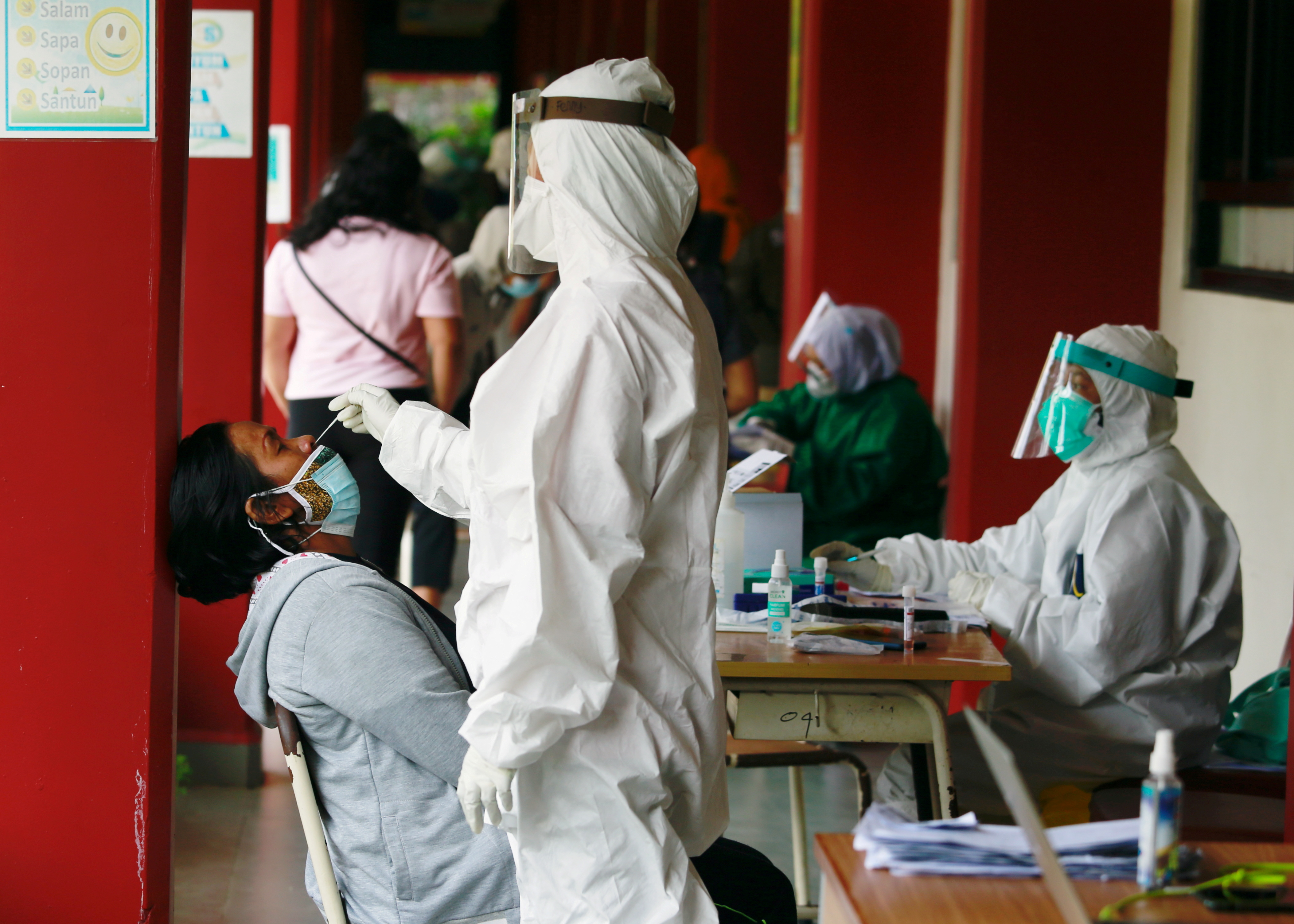 A healthcare worker in personal protective equipment takes a swab sample from a person to test for the coronavirus disease (COVID-19) during mass testing at a school in Jakarta