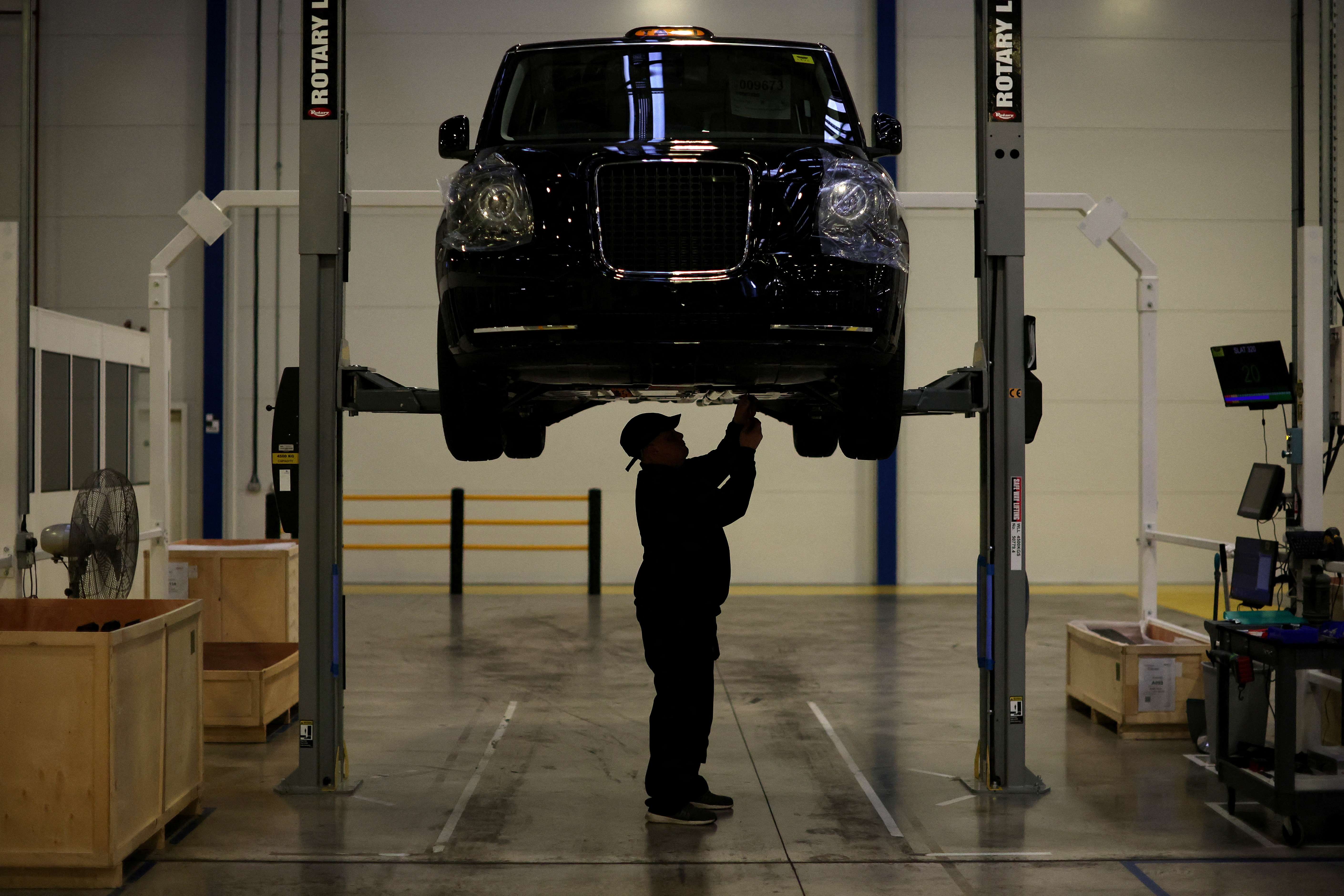 A worker stands beneath a Texas Electric taxi inside the LEVC (London Electric Vehicle Company) factory in Coventry
