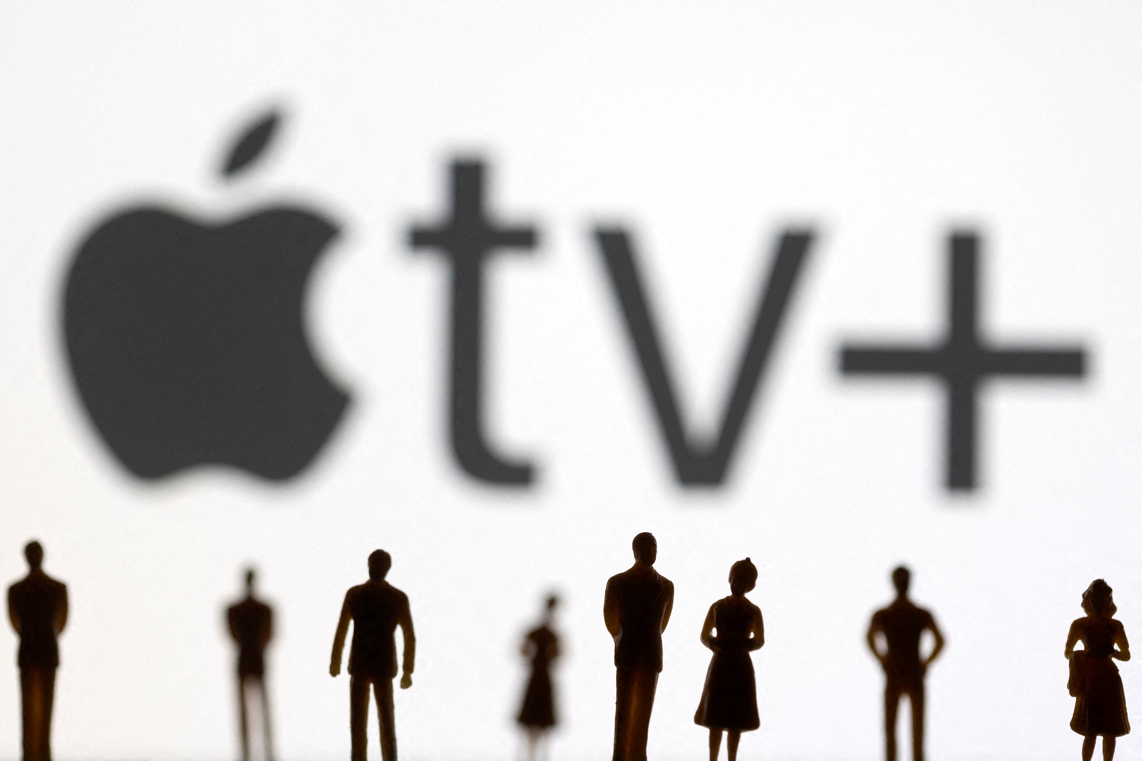 Toy figures of people are seen in front of the displayed Apple TV + logo, in this illustration