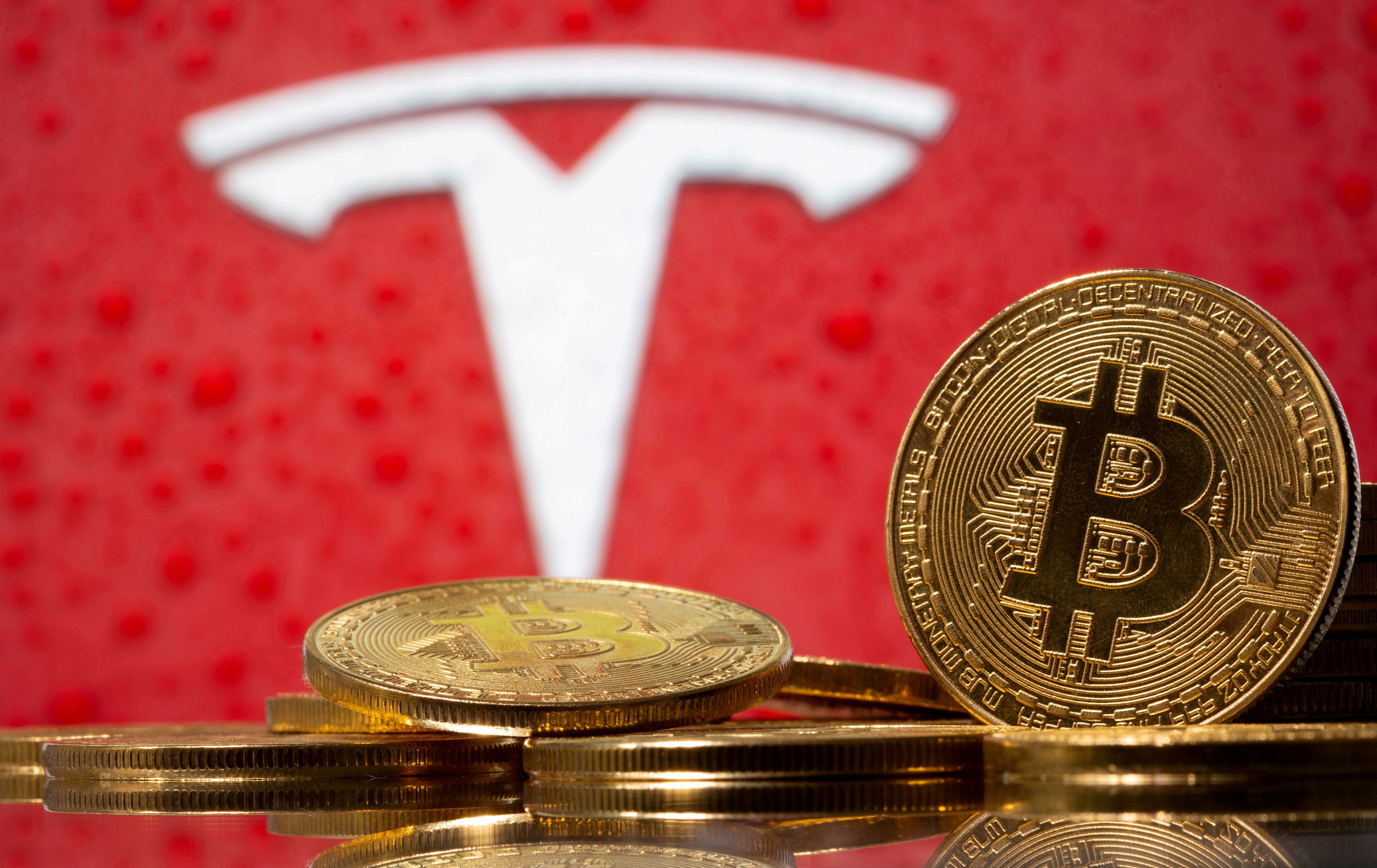 Representations of virtual currency bitcoin are seen in front of Tesla logo in this illustration