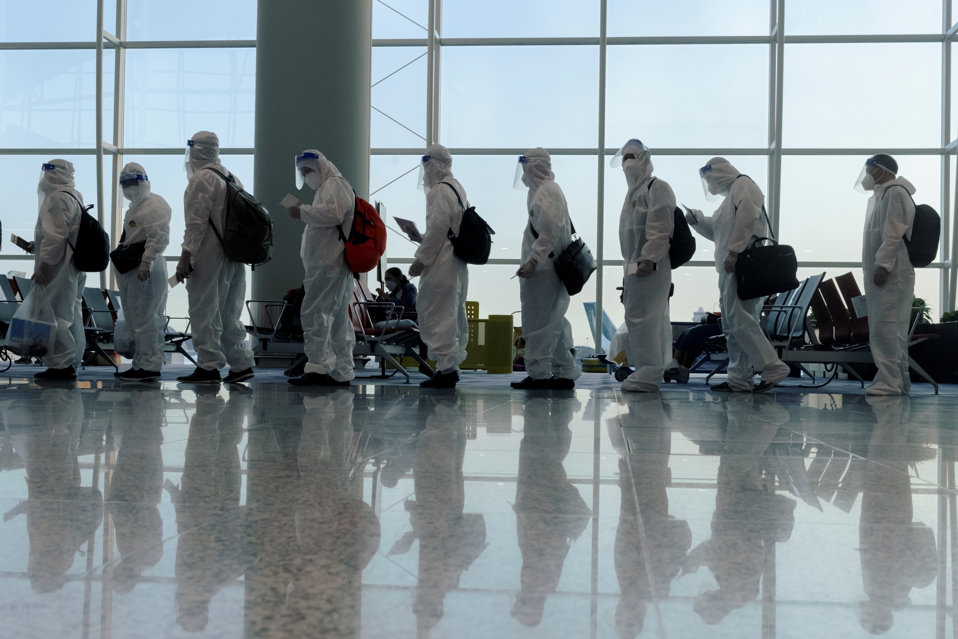 Passengers wearing protective suits (PPE) line up to board their plane for an international flight at Hong Kong airport