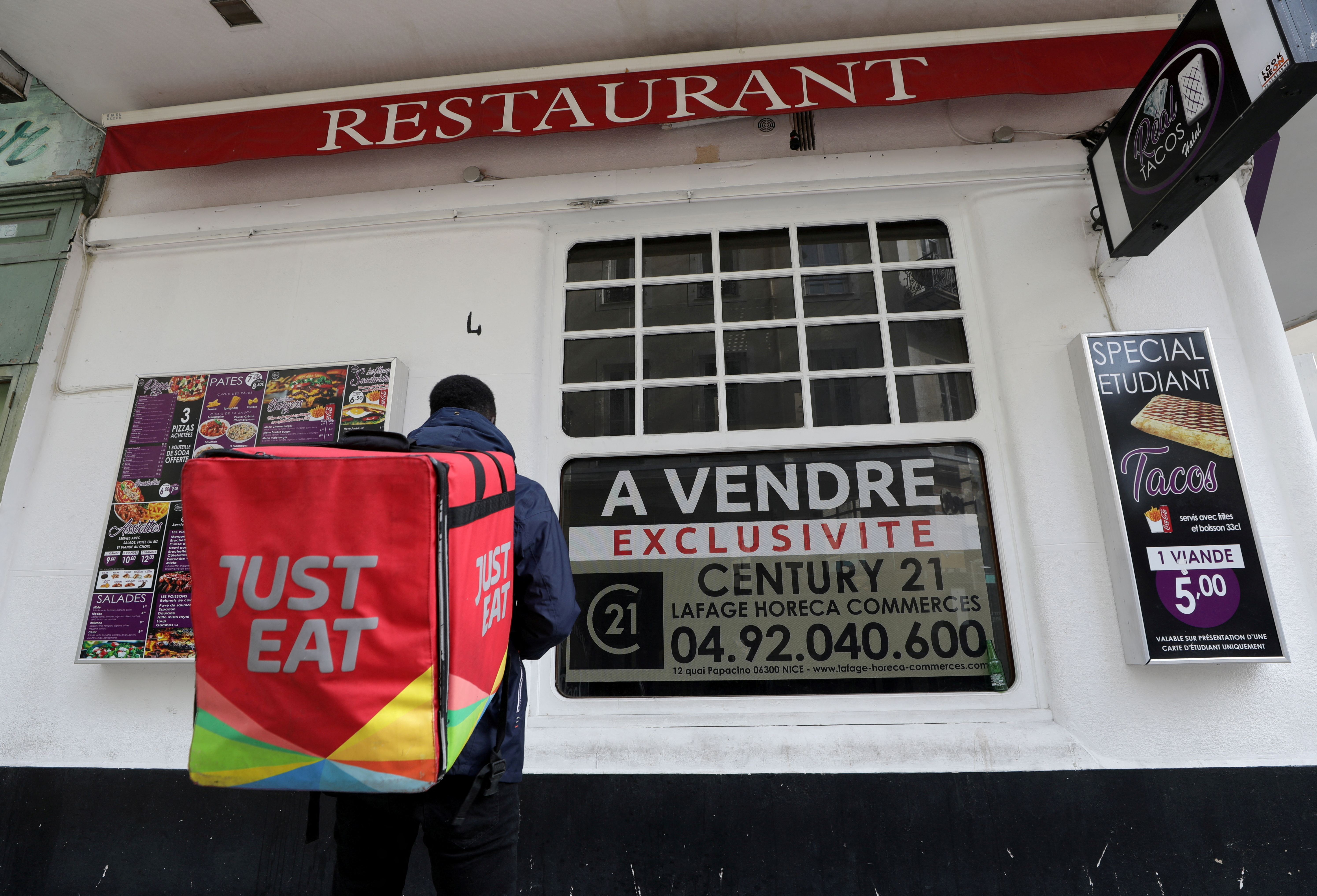 A Just Eat delivery man stands in front of a closed restaurant on sale in Nice