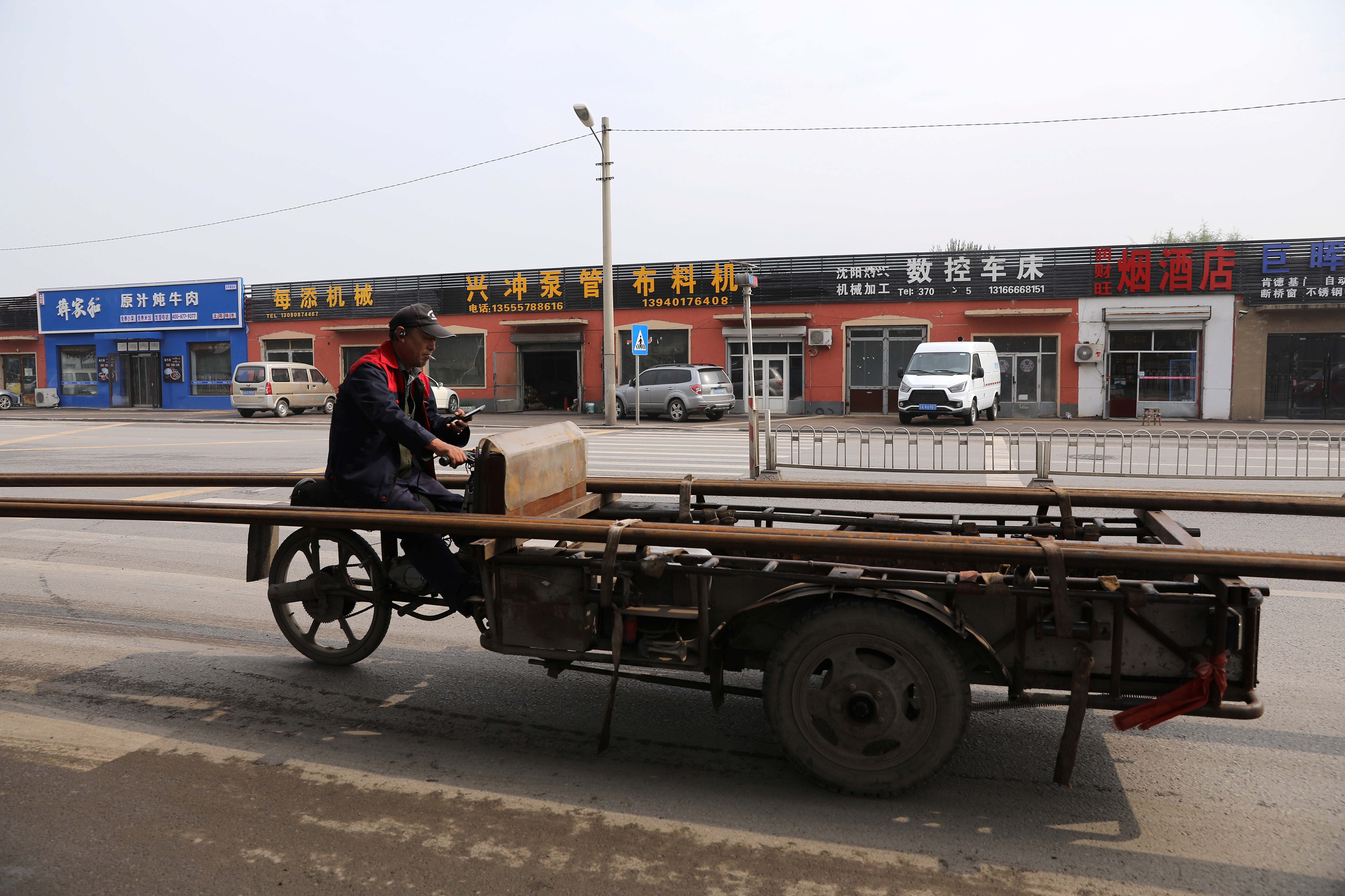 A worker rides on a vehicle carrying pipes past an industrial park in Shenyang