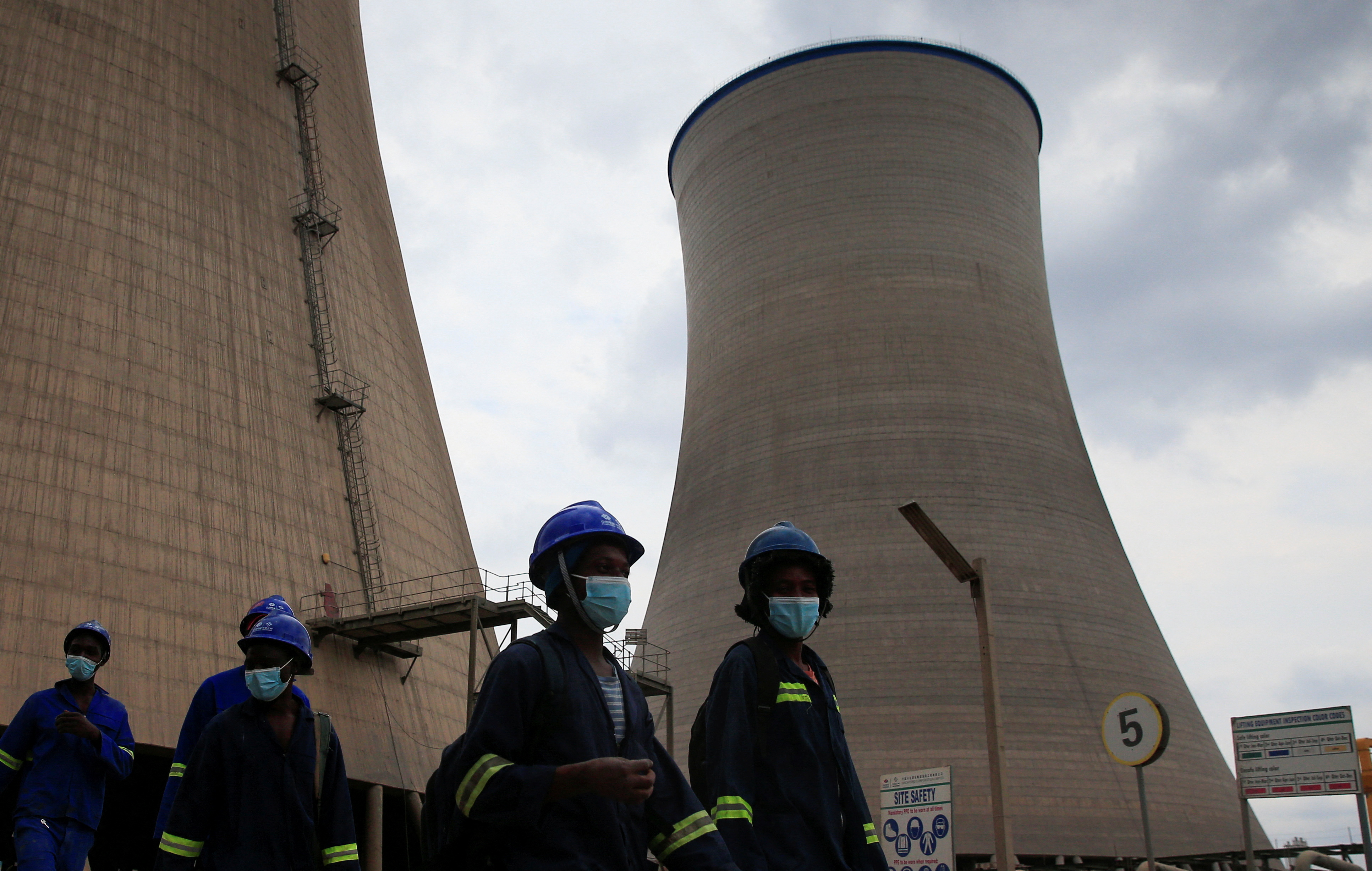 Workers walk beneath cooling towers at Hwange Power station's Phase 8, in Hwange