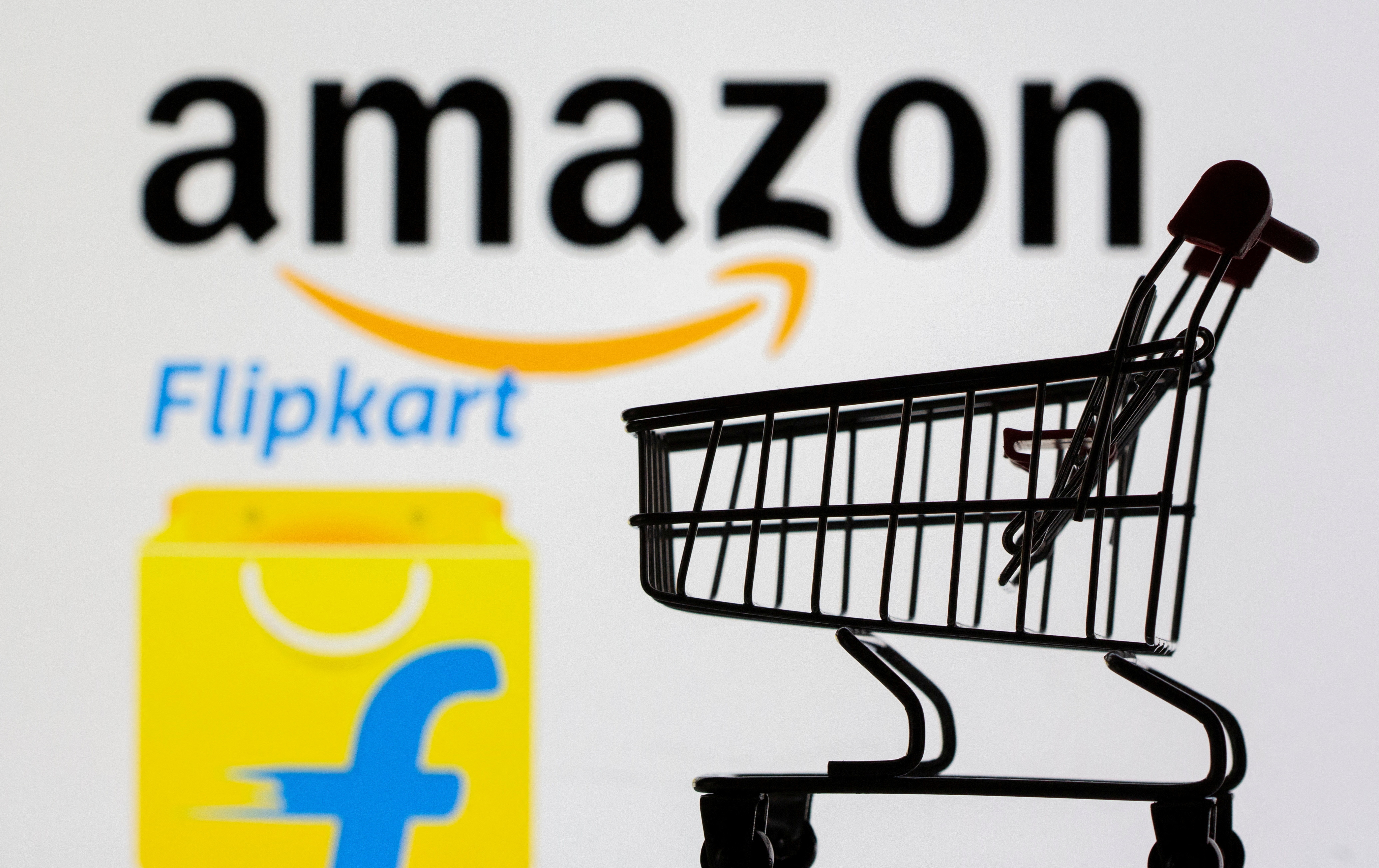 Small toy shopping cart is seen in front of displayed Amazon and Flipkart logos in this illustration